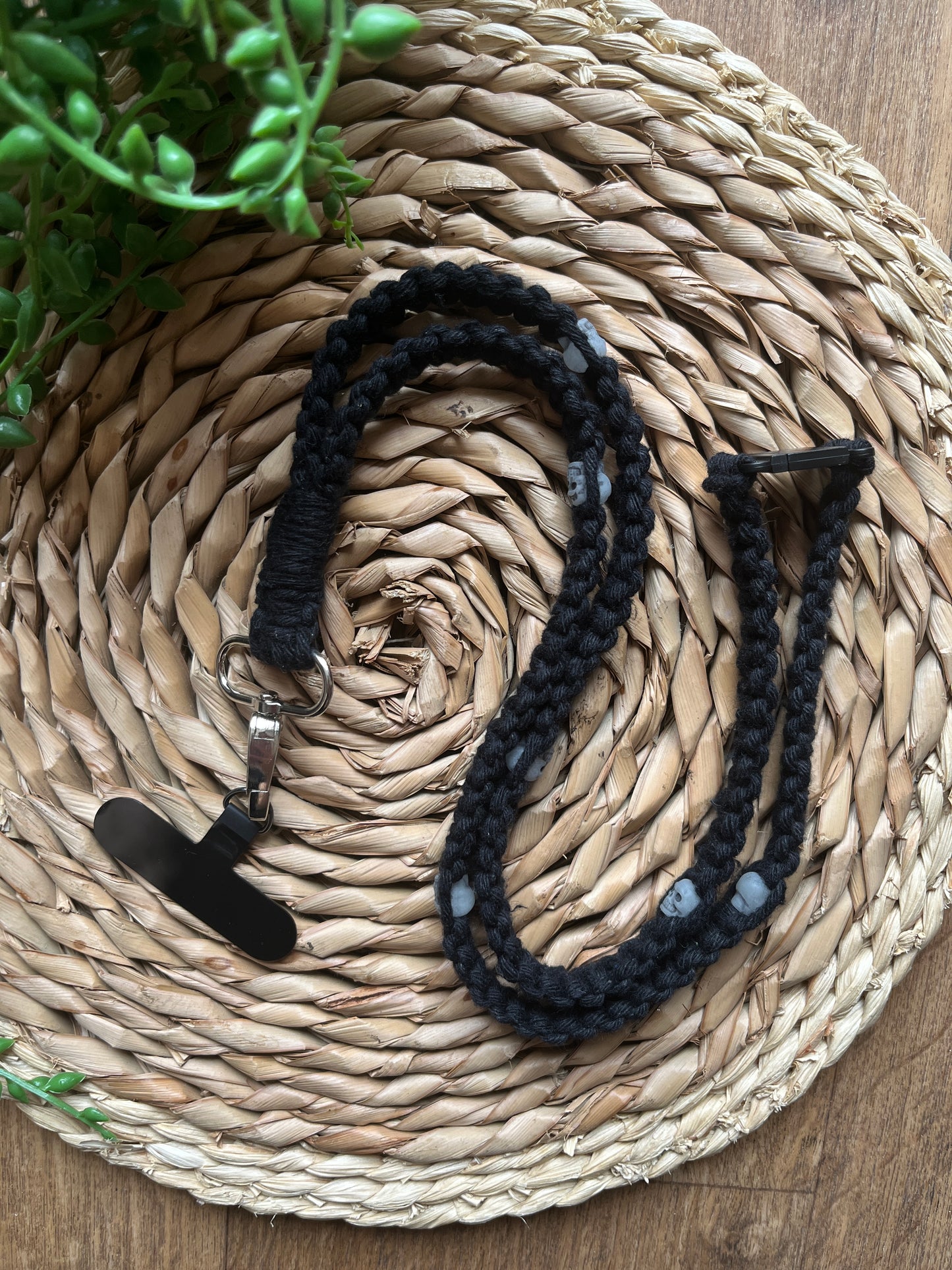 A handmade macrame phone lanyard made with black yarn, small metal skull beads and a metal clasp.
