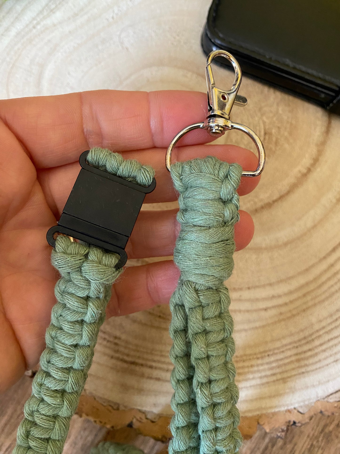 A hand showing the black plastic safety break clasp and metal clasp on a macrame phone holder lanyard made with eucalyptus green yarn.