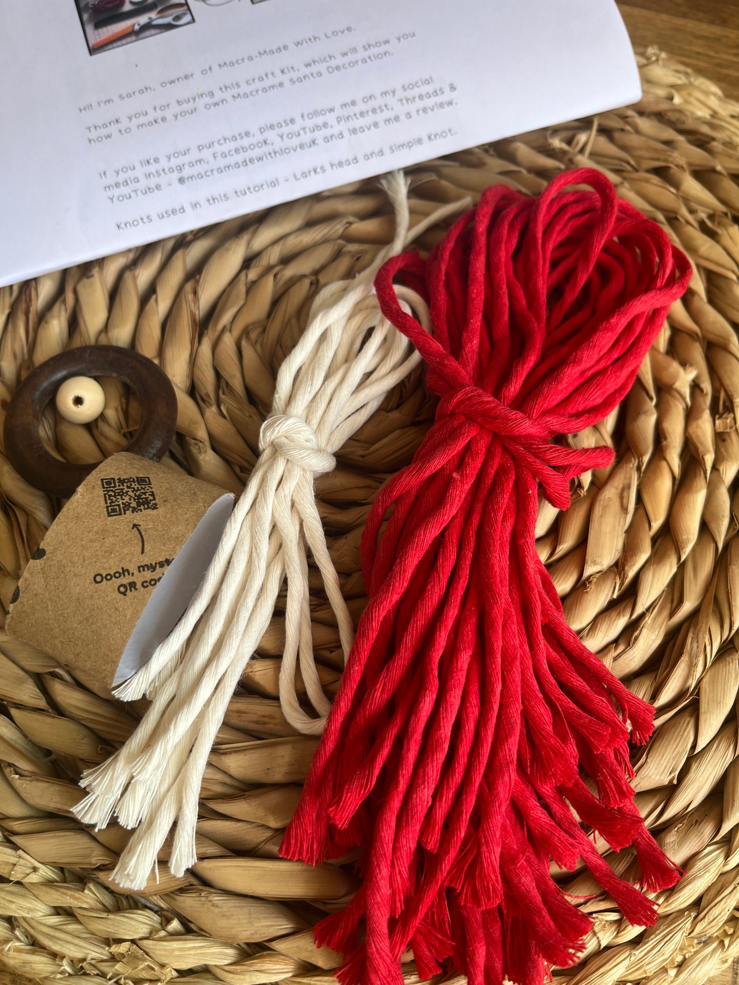 Red and white yarn and other craft supplies on a woven mat with printed instructions in the background