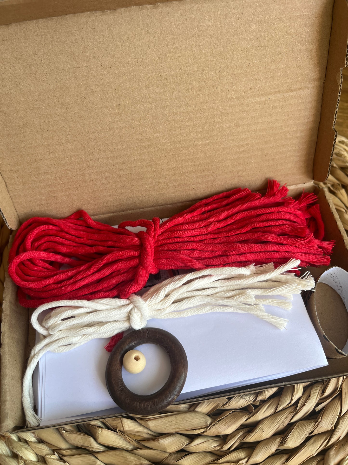 Red and white yarns with a wooden ring and bead in an open cardboard box.