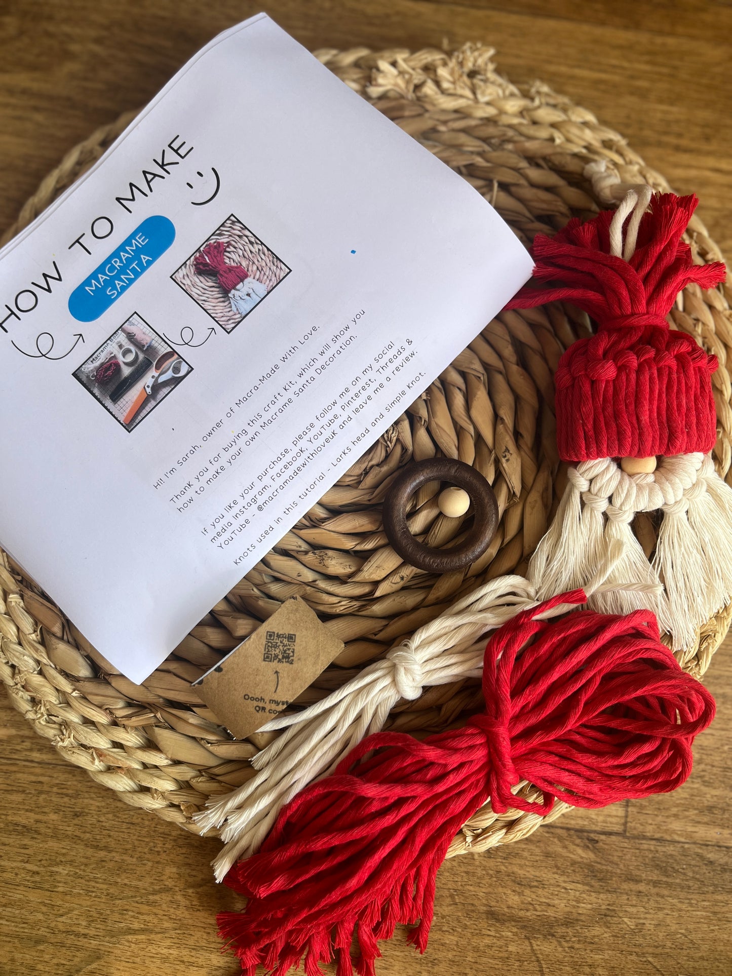 Craft kit with instructions & yarn on a woven mat next to a finished macrame santa decoration.
