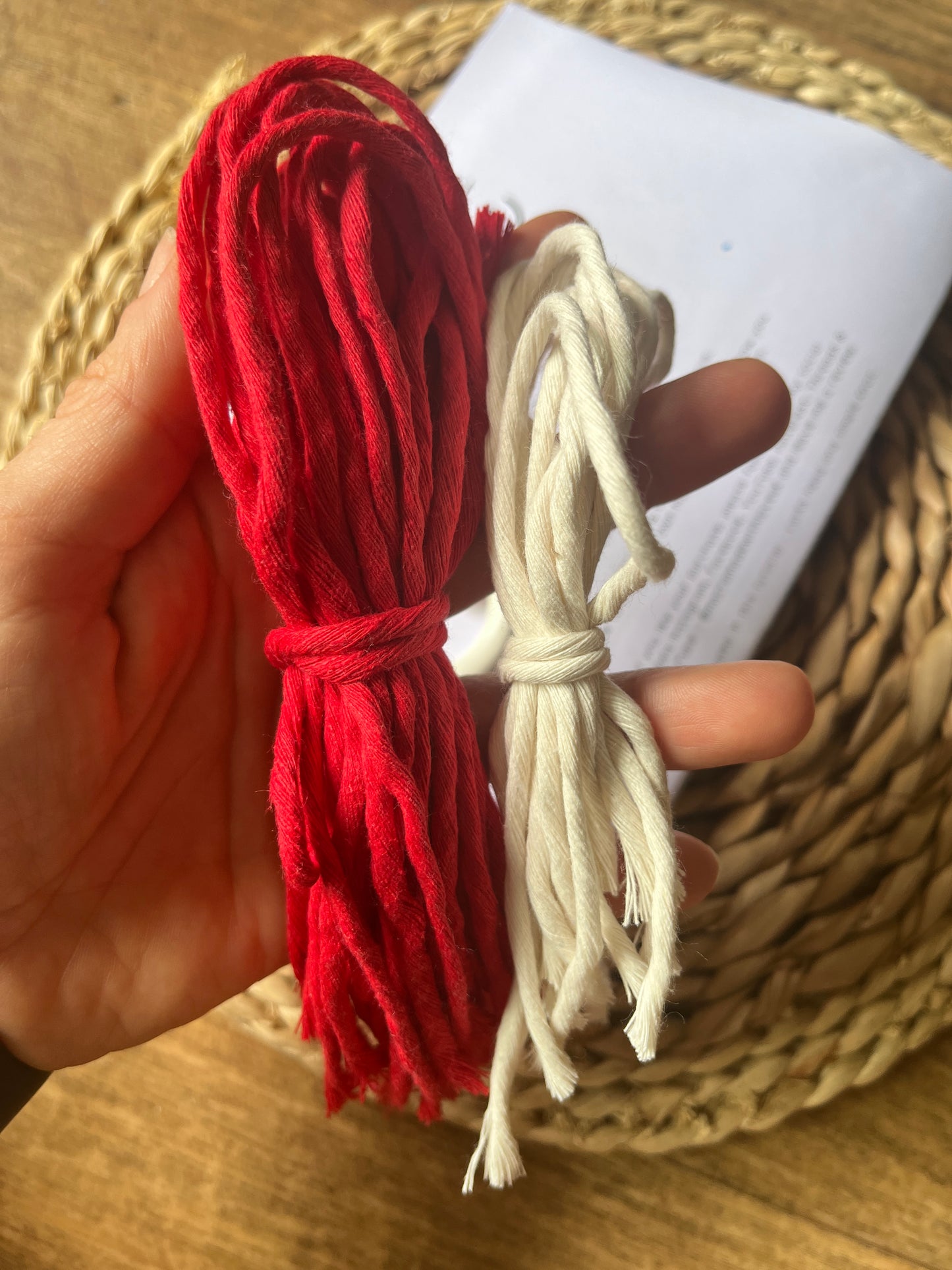 Red and white yarn held by a hand over a woven surface