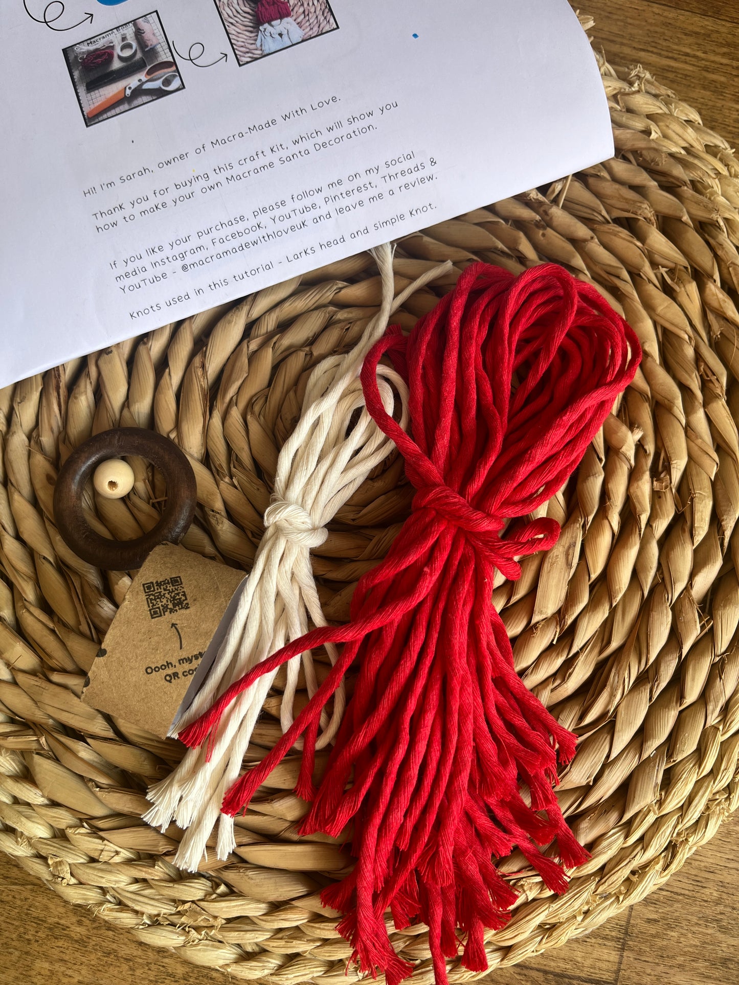 Red and white yarn bundle on a woven mat with a wooden ring and printed instructions for a DIY craft kit.