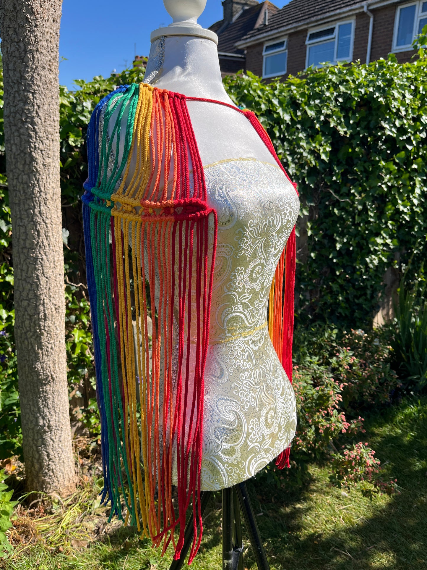 A mannequin stands outside with a handmade macrame shoulder accessory epaulette on it.