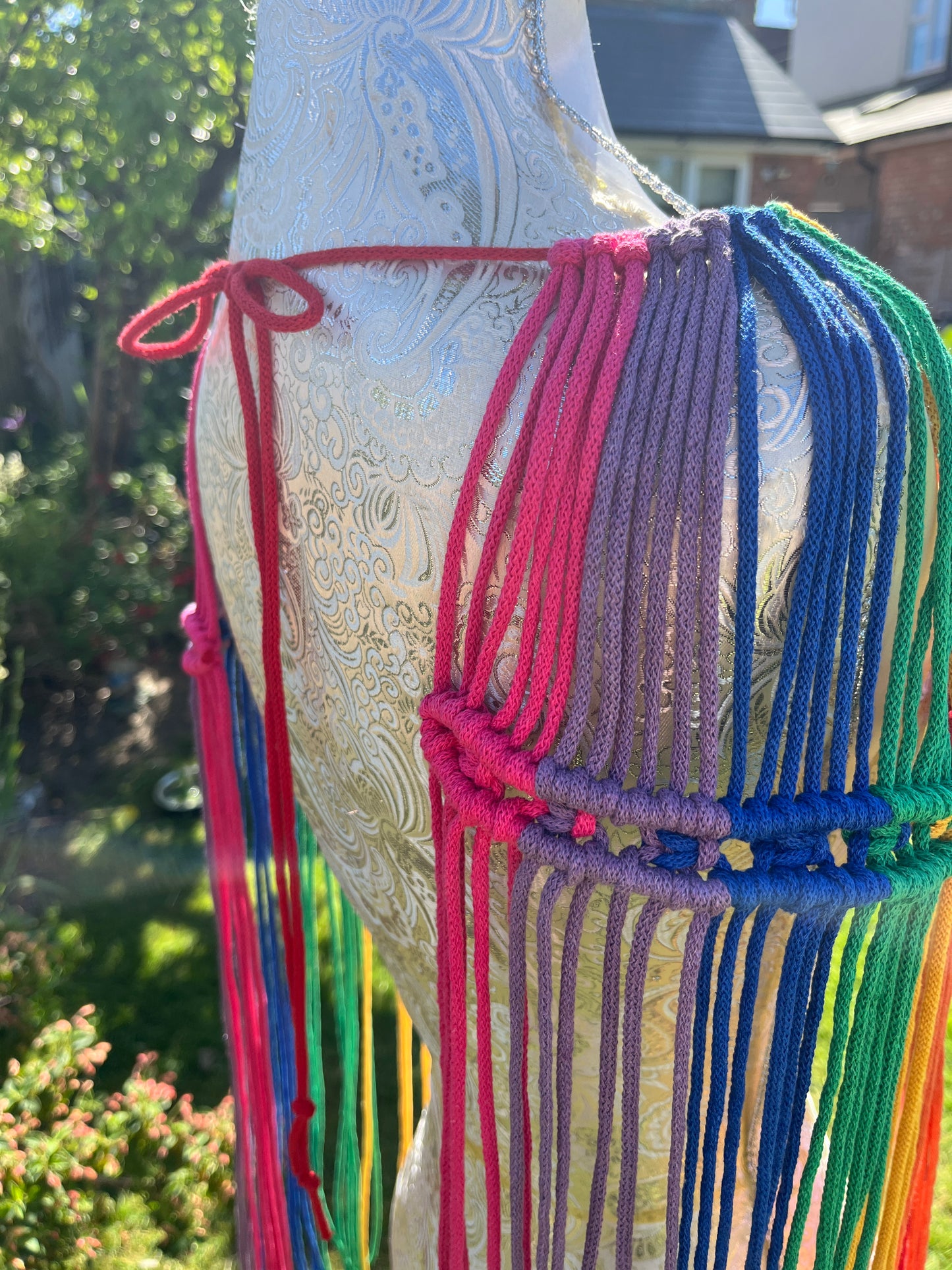 A mannequin stands outside in the sunshine, with a handmade macrame shoulder accessory epaulette across it.
