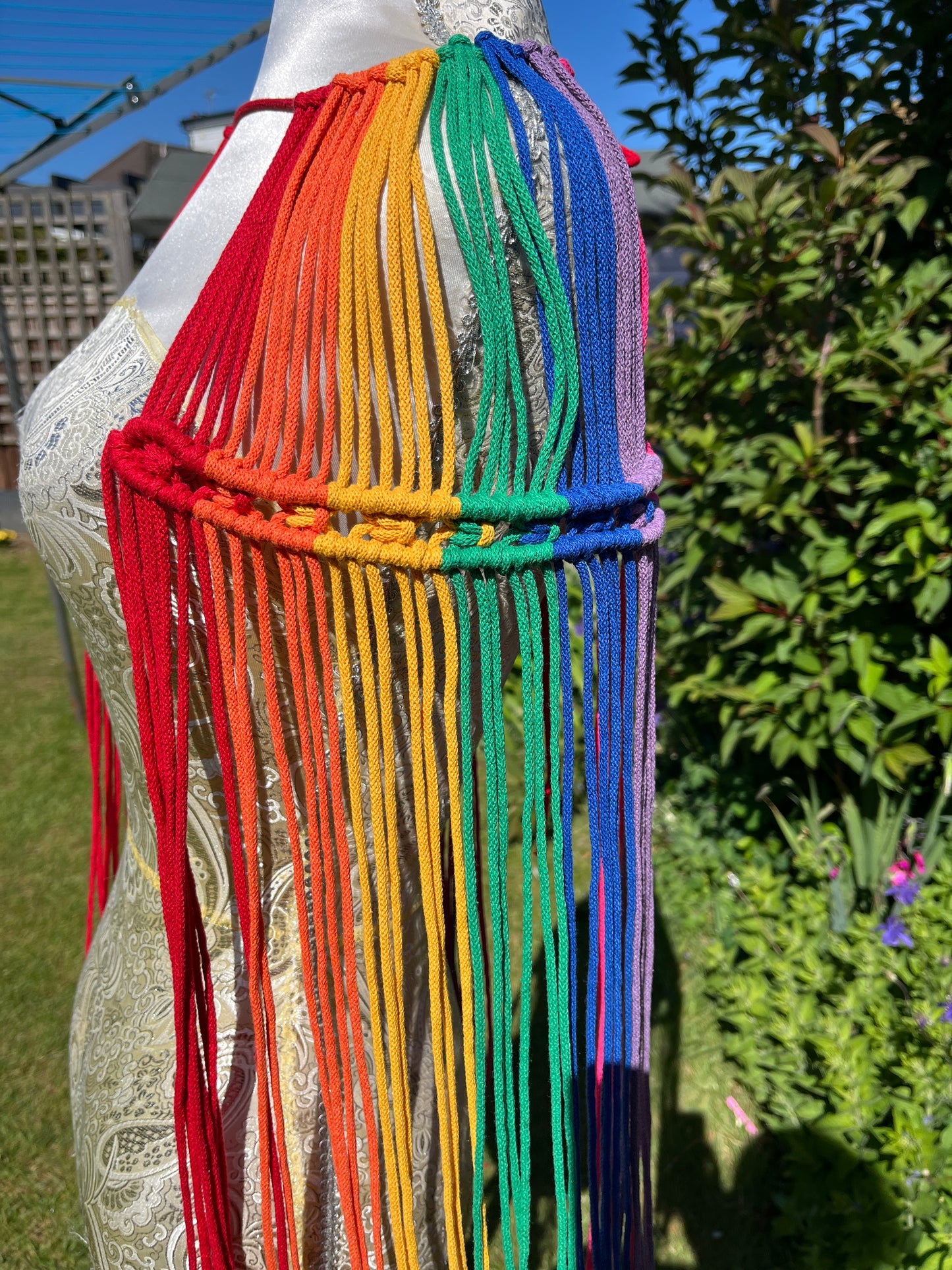 A mannequin stands outside with a handmade macrame shoulder accessory epaulette on it.