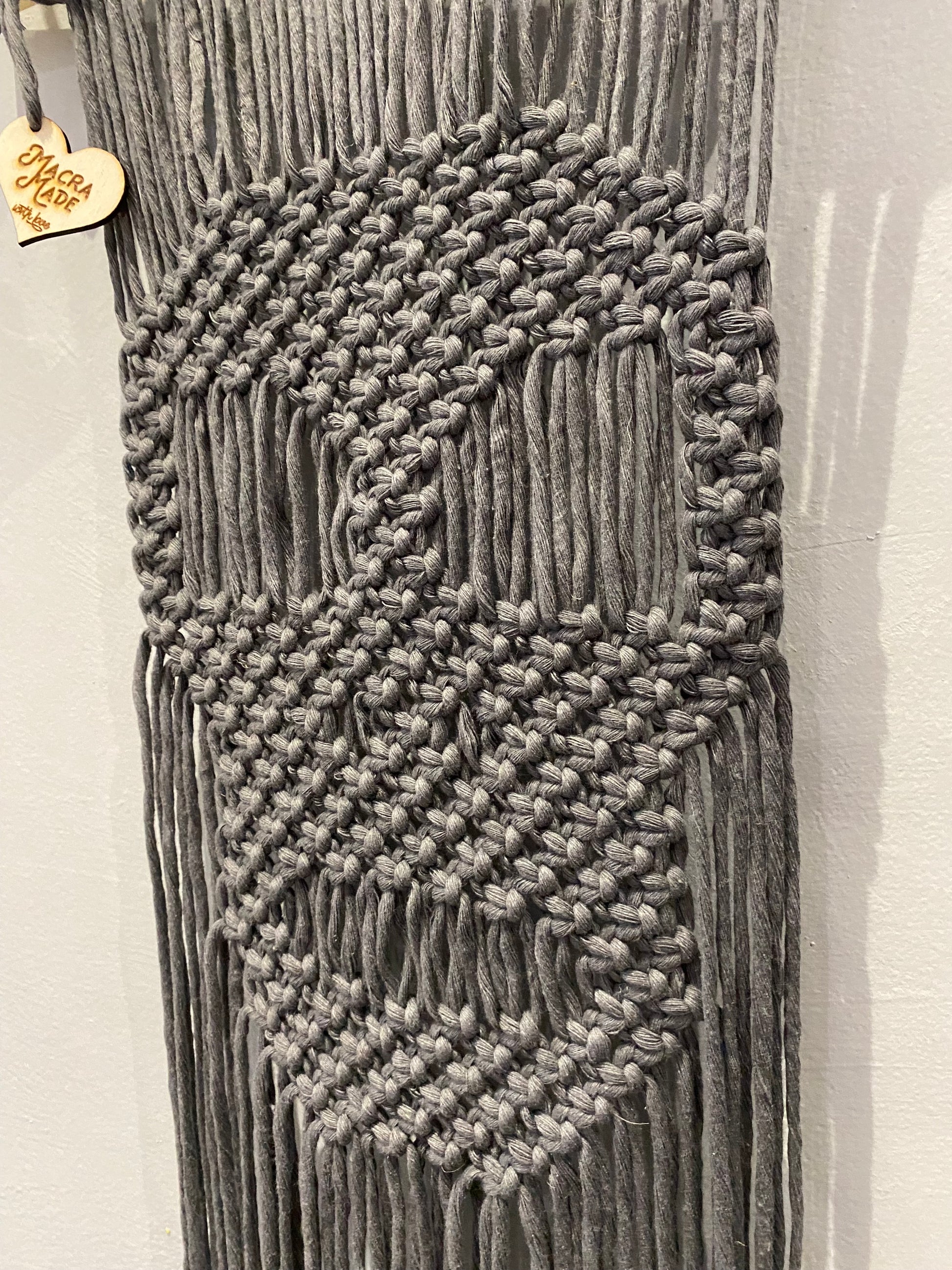 Close up of a dark grey macrame wall hanging with a knotted pattern in the shape of a skull.