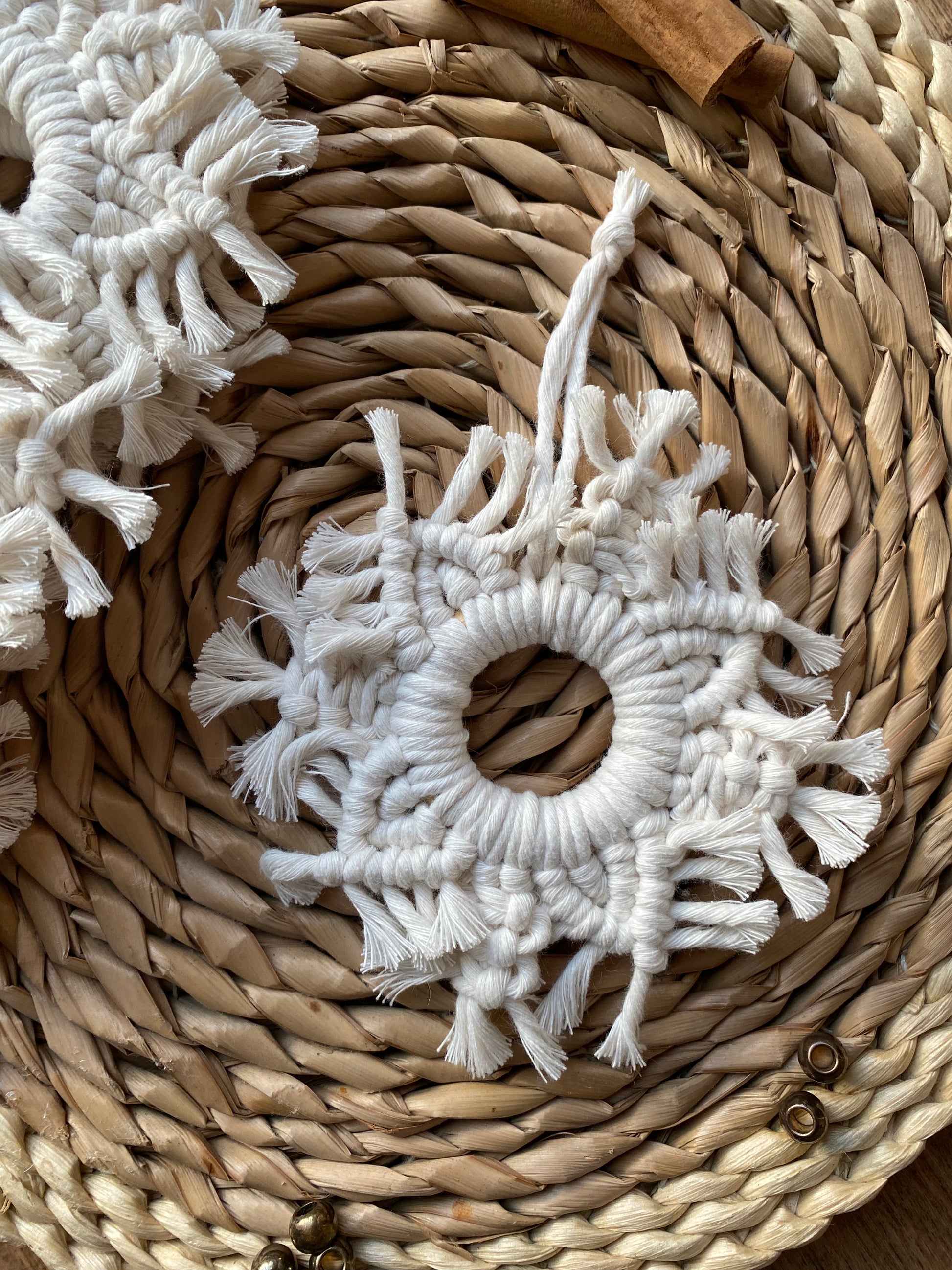 A handmade macrame snowflake ornament, knotted with natural coloured cotton yarn, on a wicker surface surrounded by cinnamon sticks and beads for decoration.