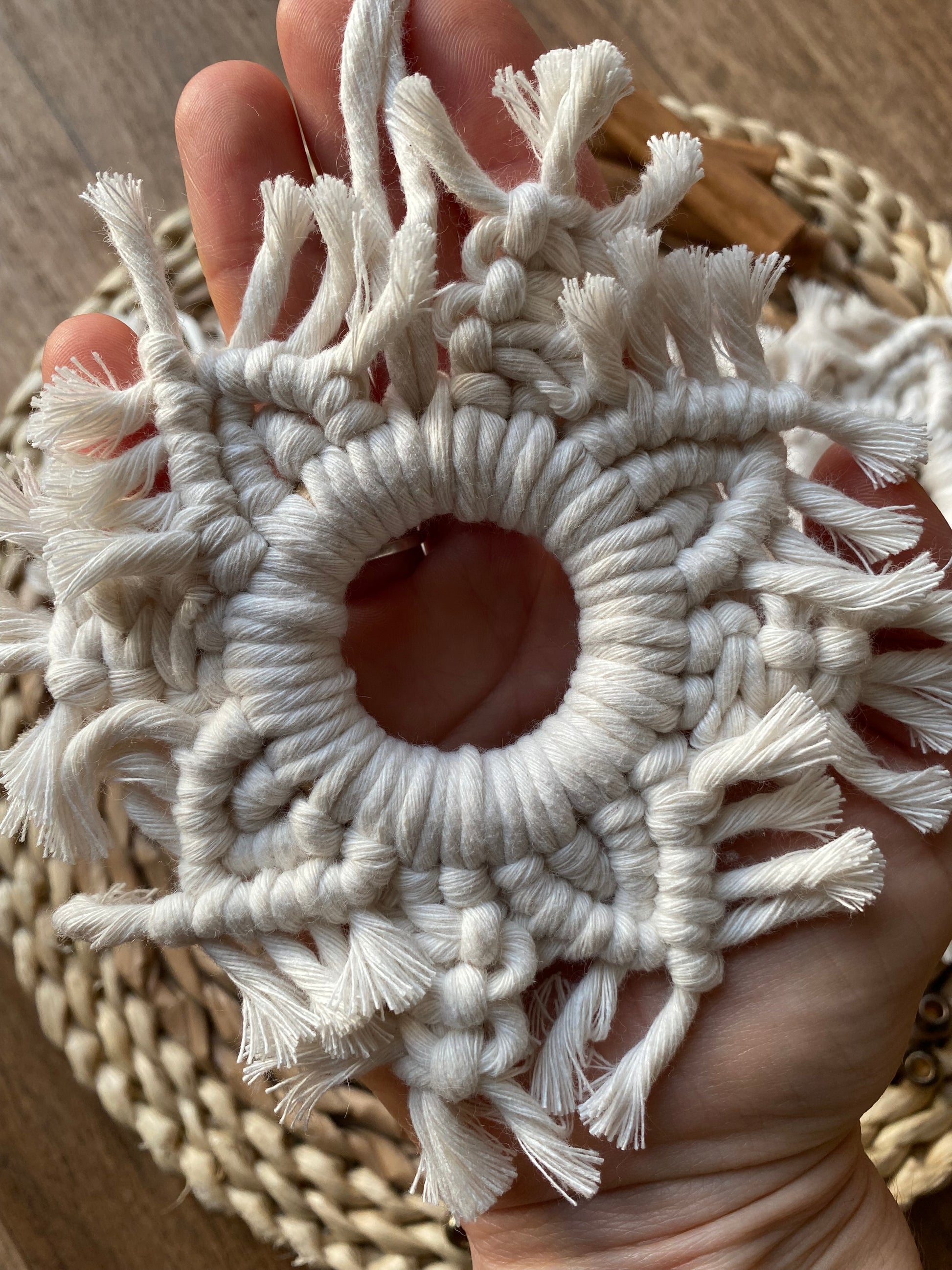 A hand holding a handmade macrame snowflake ornament, knotted with natural coloured cotton yarn.