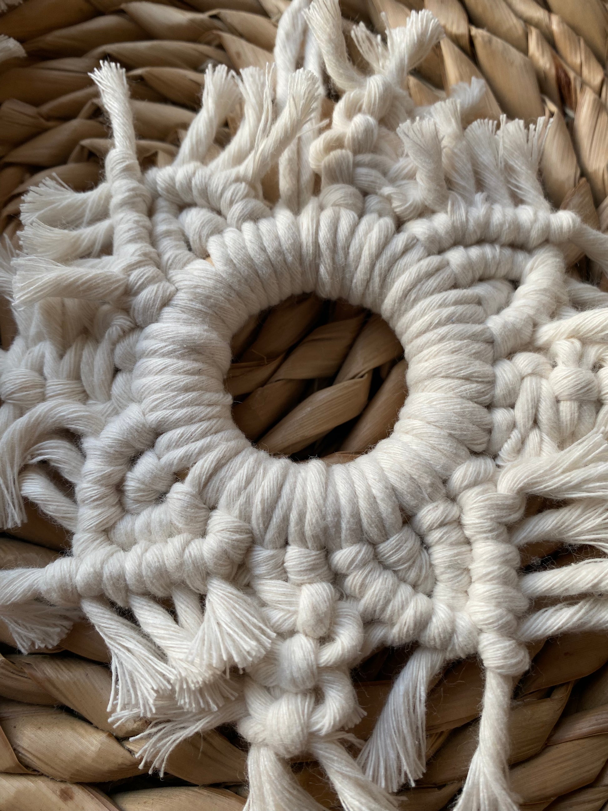 A close up image of a handmade macrame snowflake ornament, knotted with natural coloured cotton yarn, on a wicker surface.