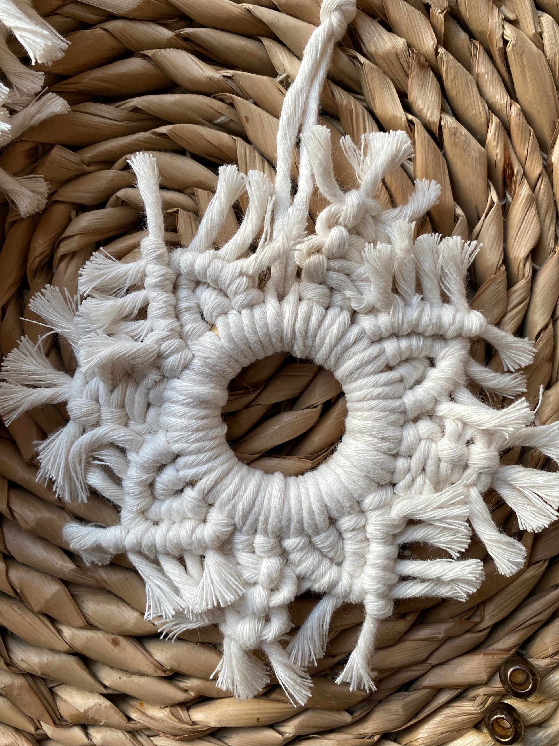 Close up of a handmade macrame snowflake ornament, knotted with natural coloured cotton yarn, on a wicker surface.