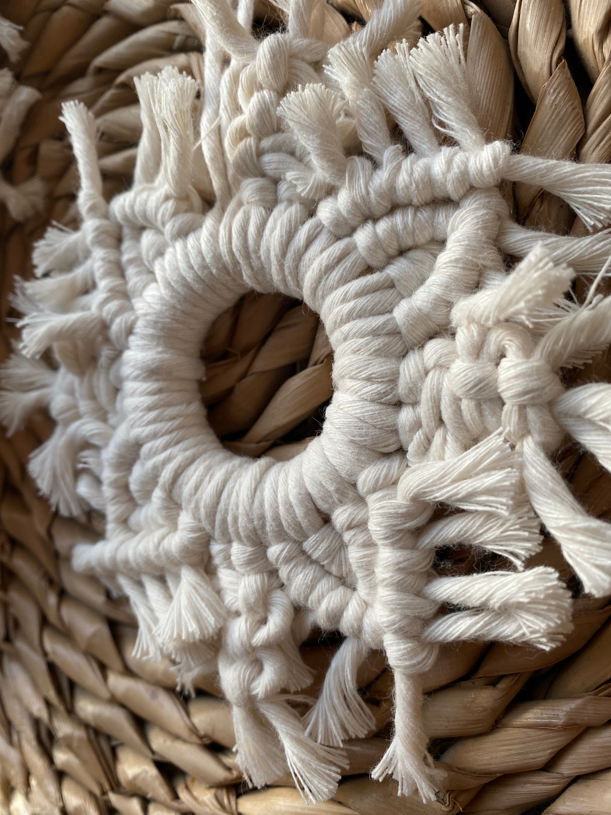 Close up angled image of a handmade macrame snowflake ornament, knotted with natural coloured cotton yarn, on a wicker surface.