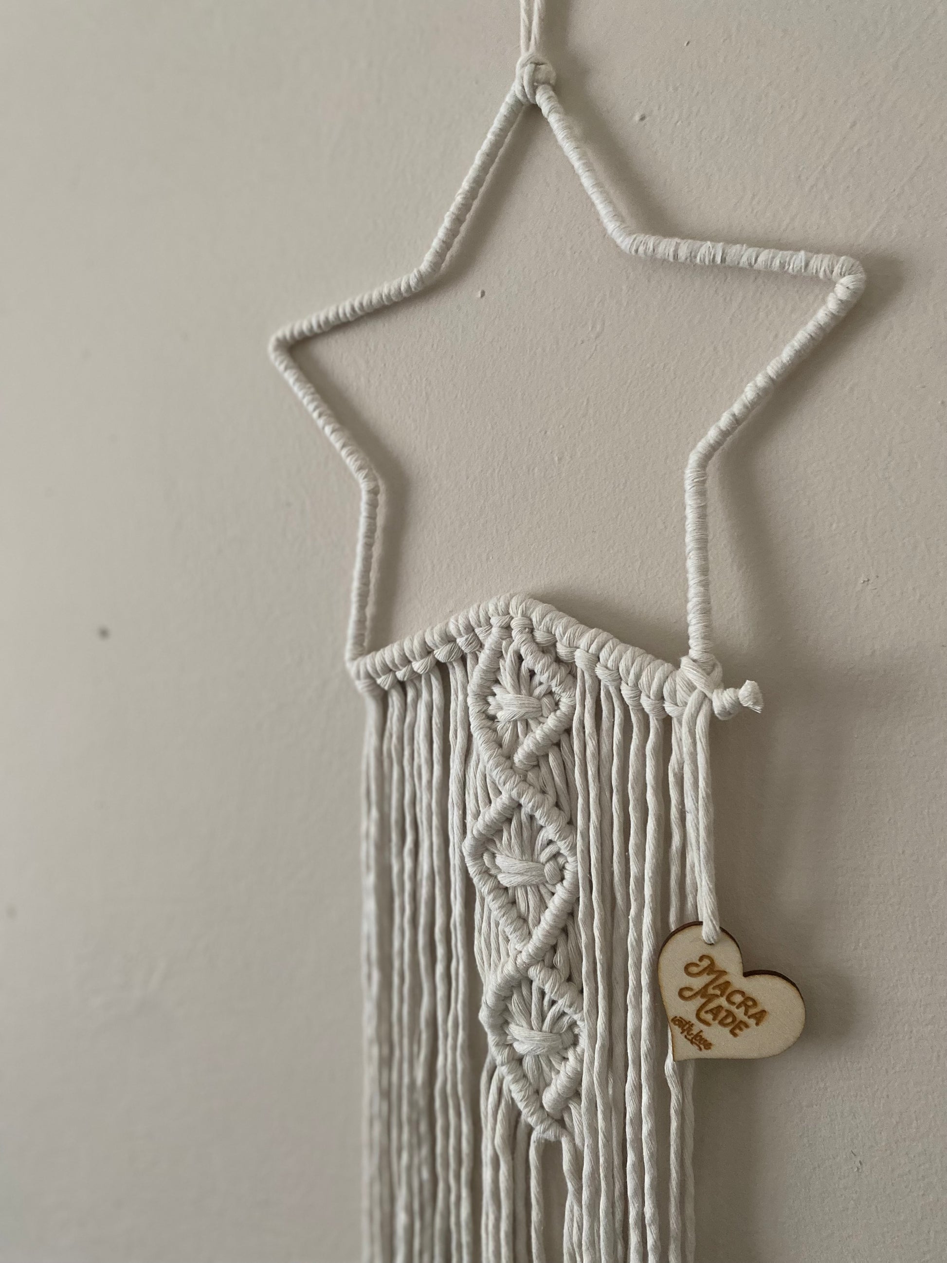 Close up of a natural star shaped macrame wall hanging with long hanging tails, hanging on a white wall.