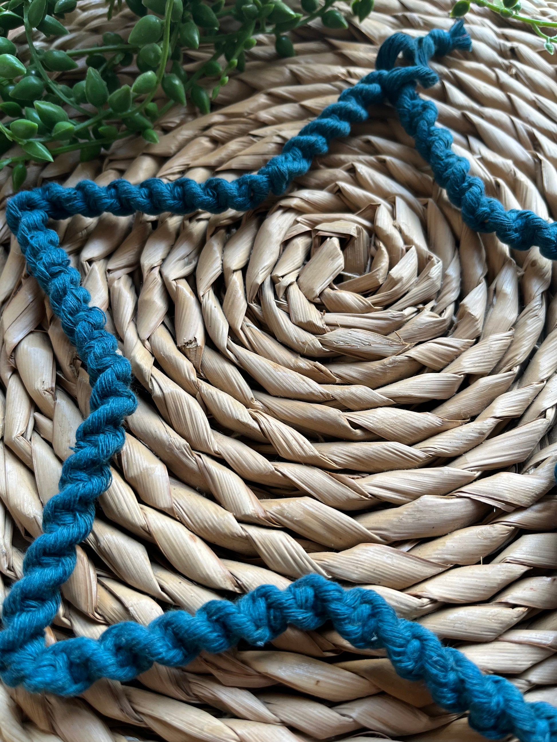 Star shaped wall hanging, wrapped in petrol blue cotton with a twisted knot pattern, on a woven mat.