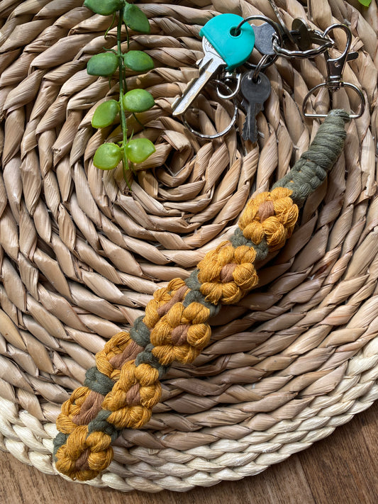 A wristlet keyring made with macrame knots in the style of yellow sunflowers with brown centres, laid on a wicker mat attached to a small set of silver keys.
