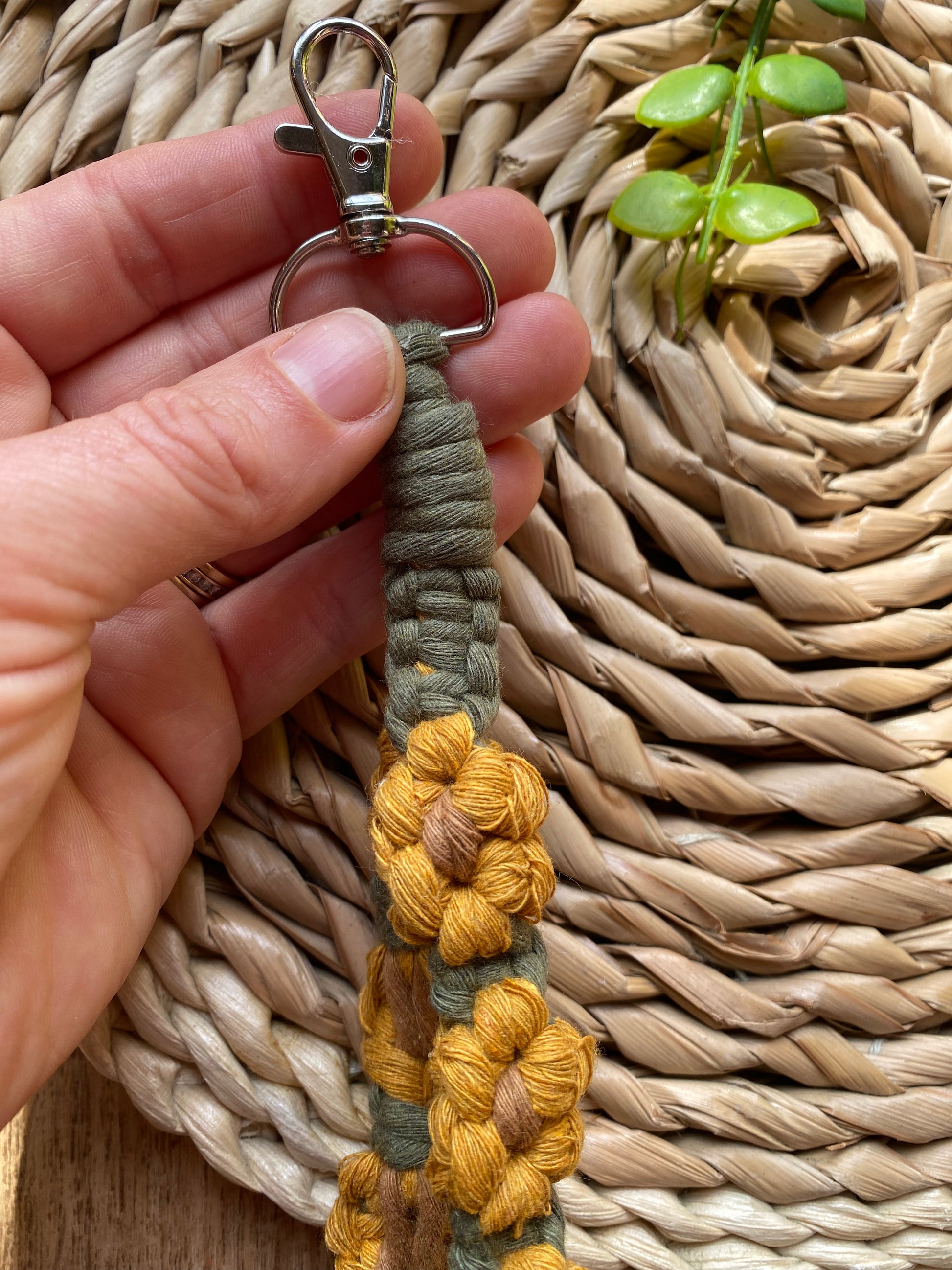 A hand holding the metal clasp on the end of a wristlet keyring made with macrame knots in the style of yellow sunflowers with brown centres.