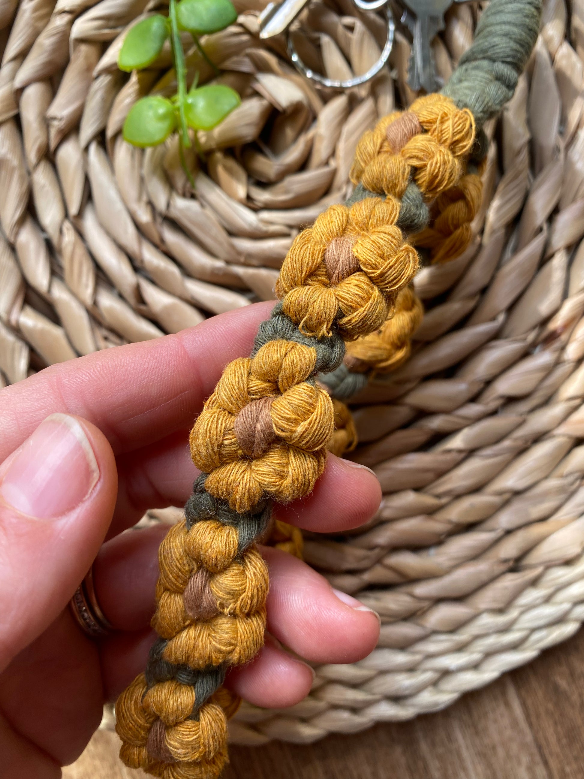 A hand holding a wristlet keyring made with macrame knots in the style of yellow sunflowers with brown centres.