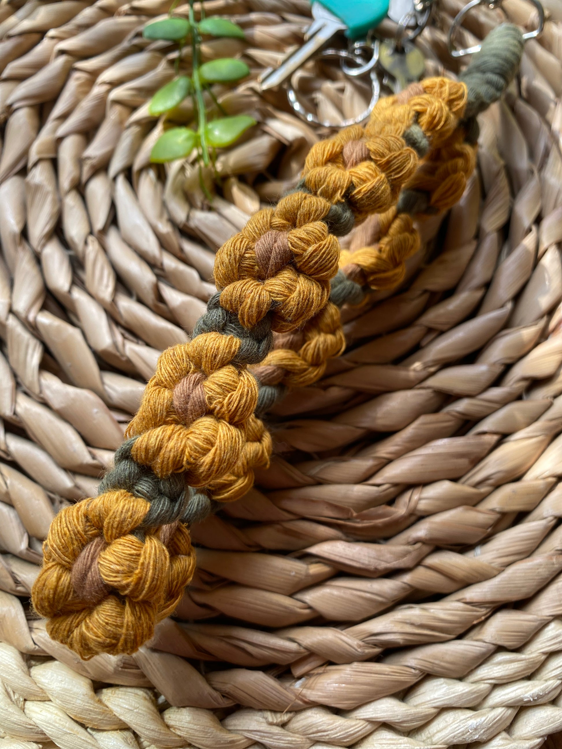 Close up of a wristlet keyring made with macrame knots in the style of yellow sunflowers with brown centres, laid on a wicker mat attached to a small set of silver keys.