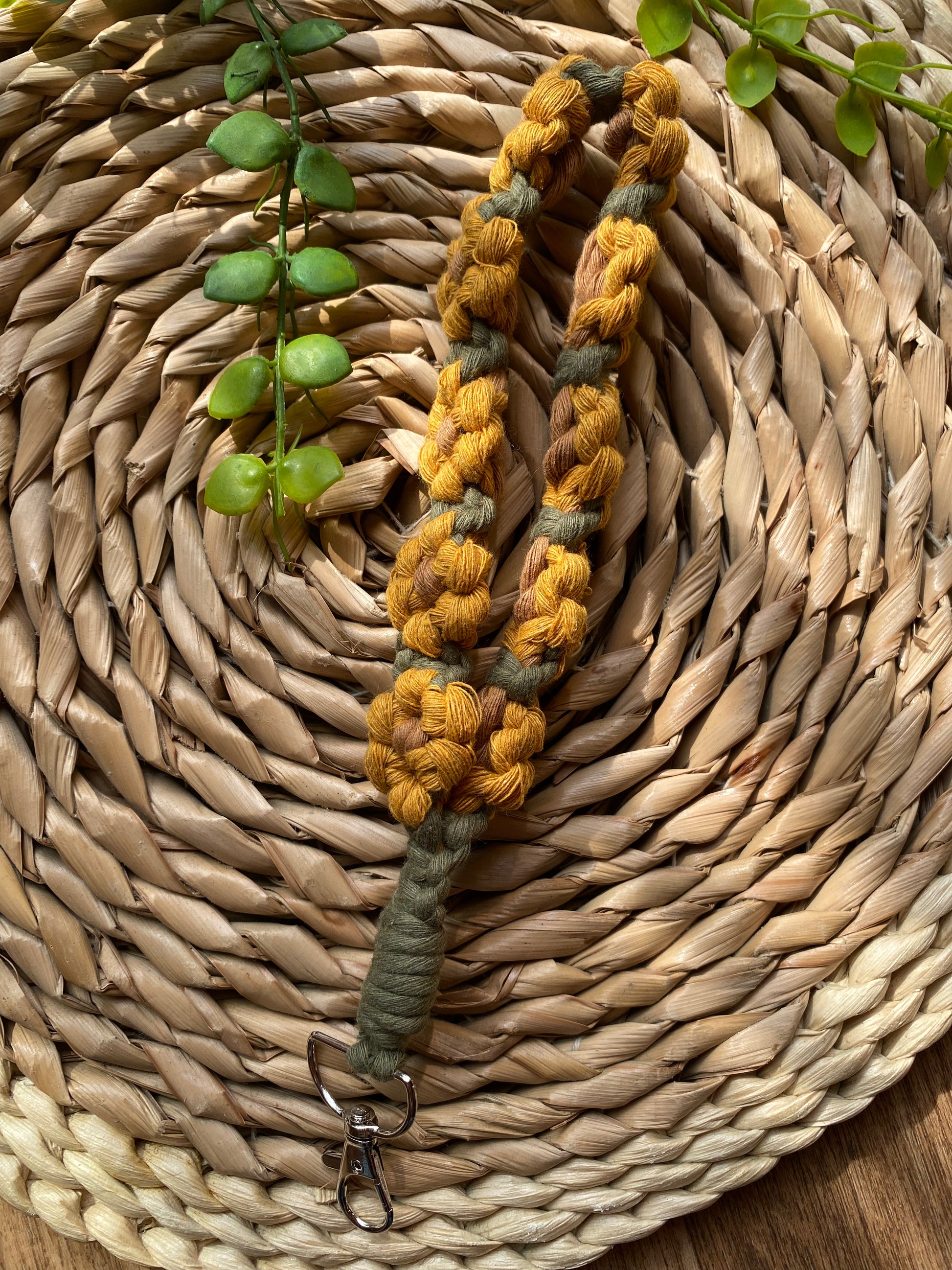 A wristlet keyring made with macrame knots in the style of yellow sunflowers with brown centres, laid on a wicker mat attached.