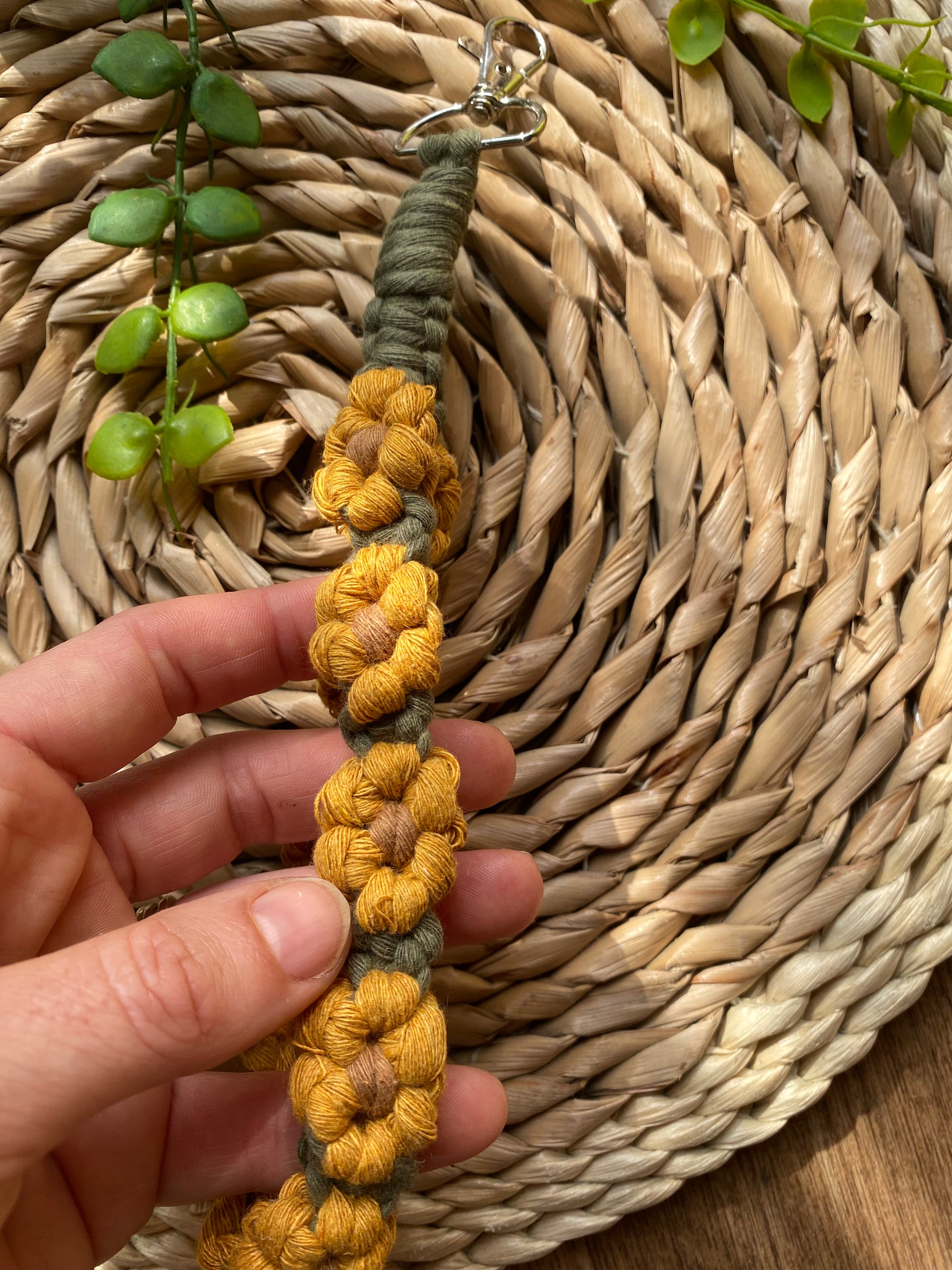 A close up of a hand holding a wristlet keyring made with macrame knots in the style of yellow sunflowers with brown centres.
