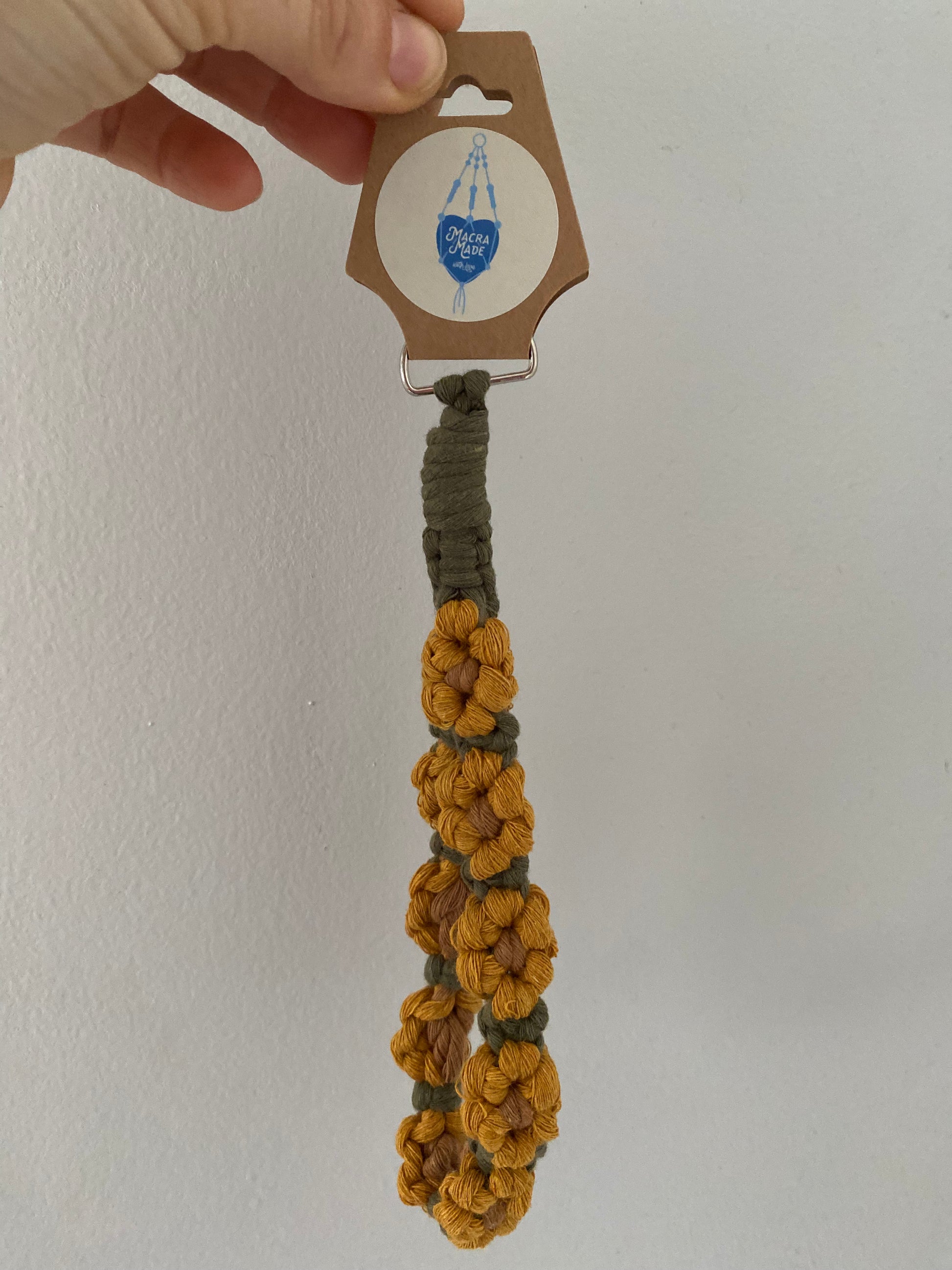 A wristlet keyring made with macrame knots in the style of yellow sunflowers with brown centres, on a cardboard swing tag.