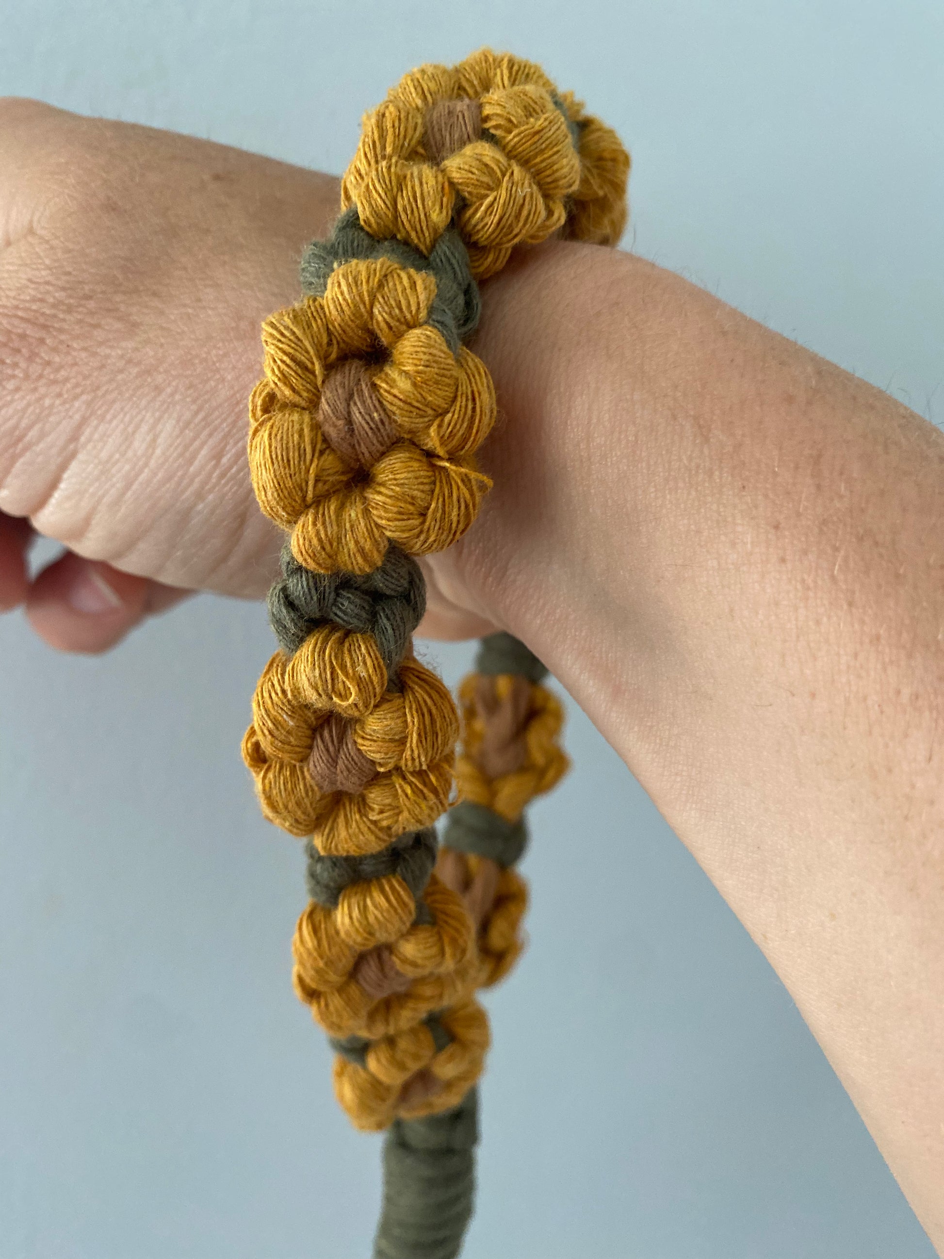 A wristlet keyring made with macrame knots in the style of yellow sunflowers with brown centres, around a woman's wrist.