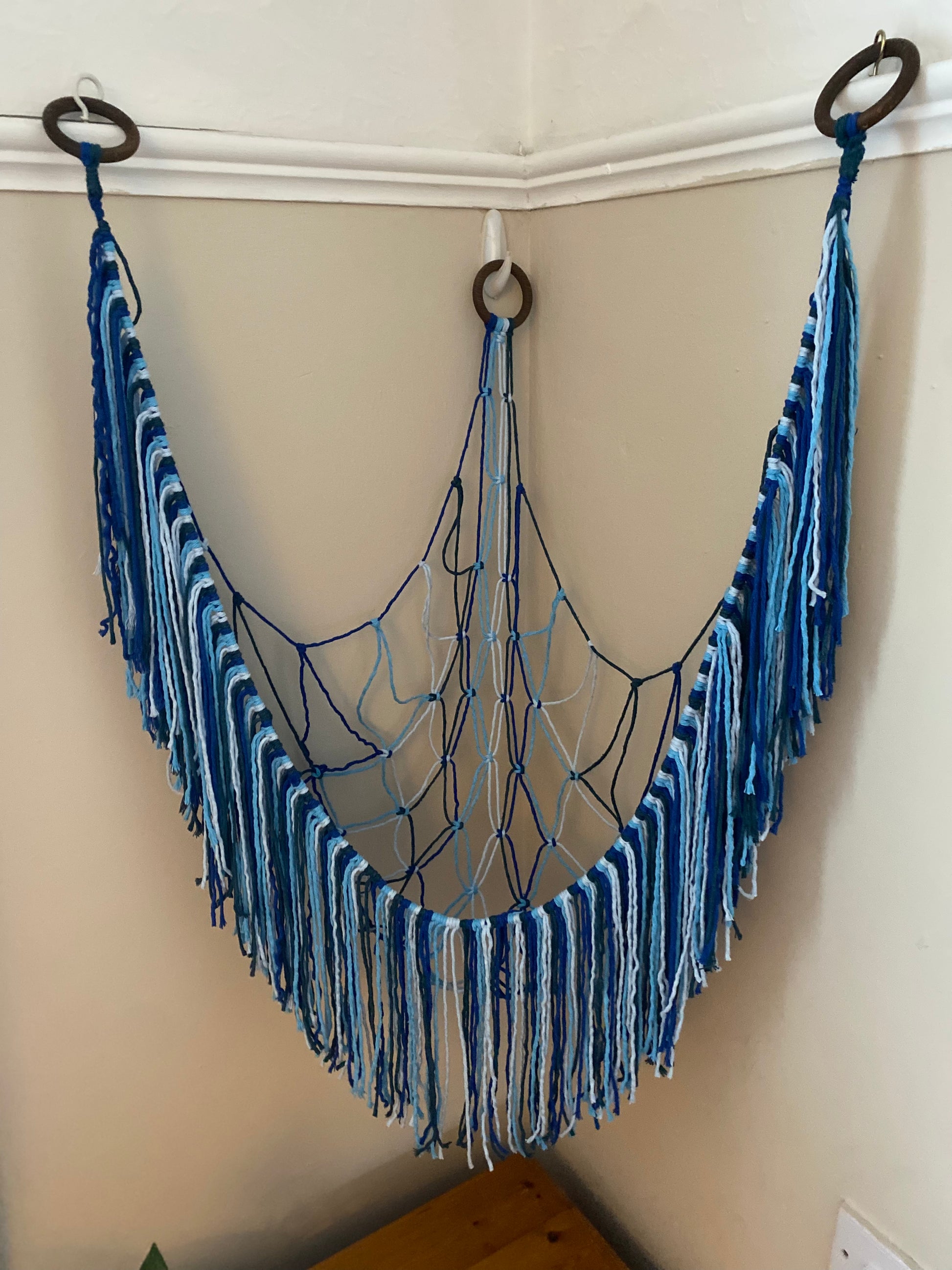 Top down view of an empty macrame toy hammock made with blue coloured yarn, with a long hanging fringe.