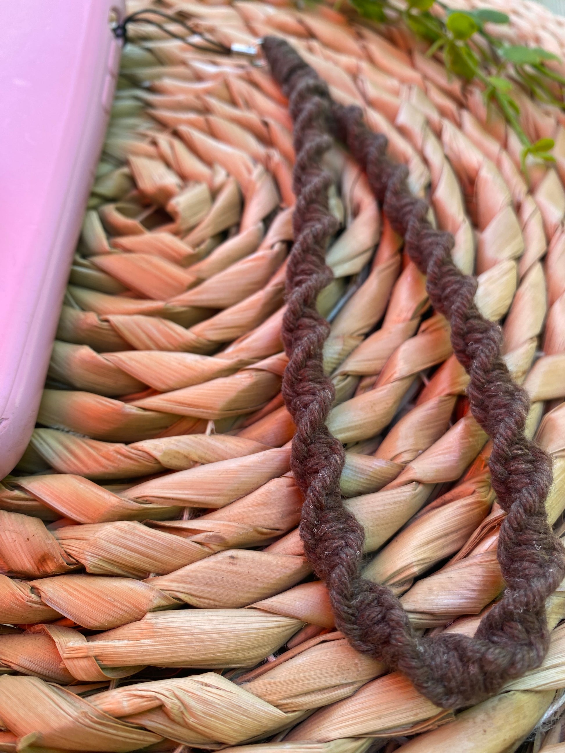 A macrame phone charm made with brown coloured yarn in a twisted knot pattern is attached to a pink phone case.