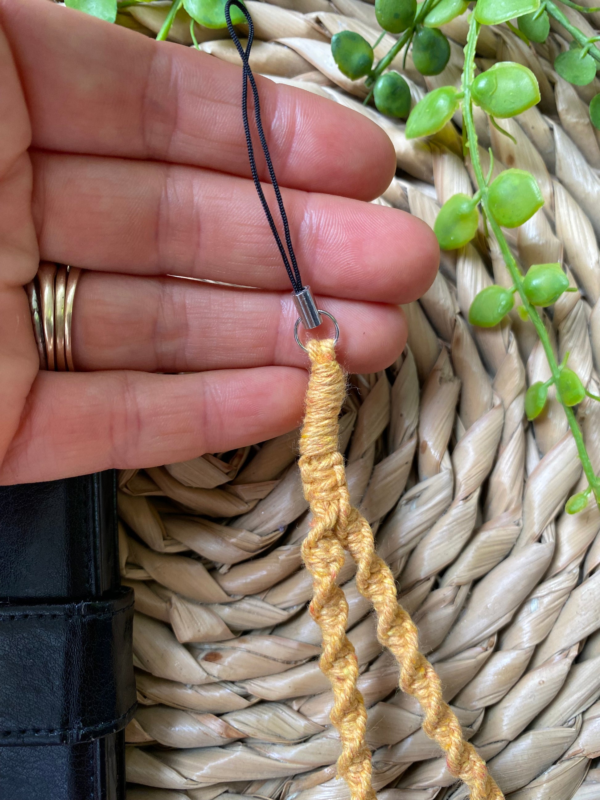 A hands holds a macrame phone charm made with yellow coloured yarn and a universal phone attachment.