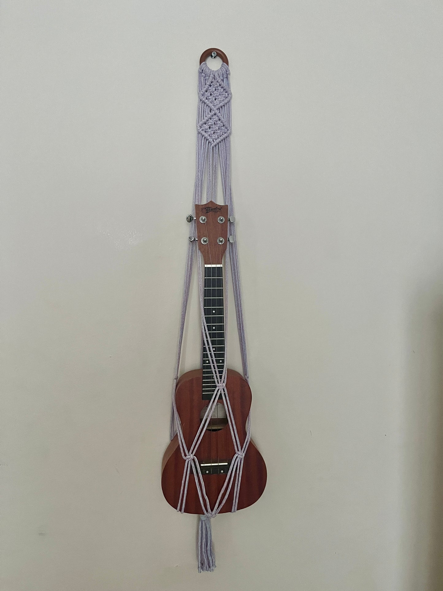 Brown ukulele securely held in a macrame strap on a beige background