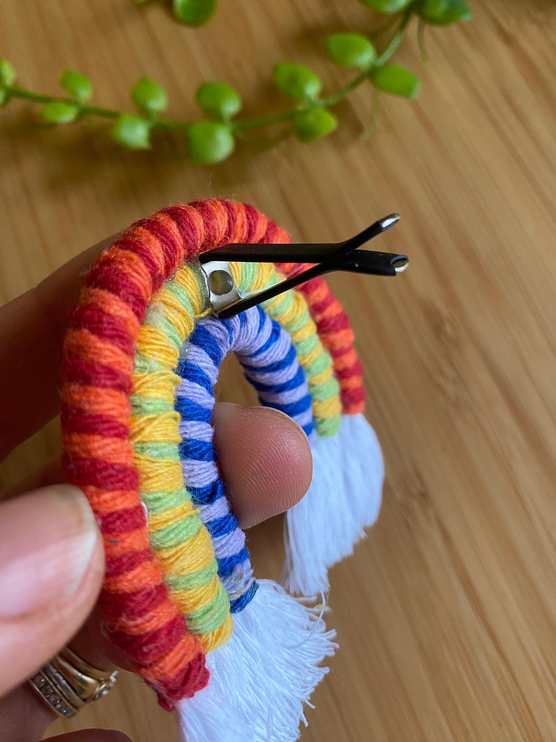 A hand holding a mini macrame rainbow, showing the reverse side where the air vent clip is attached