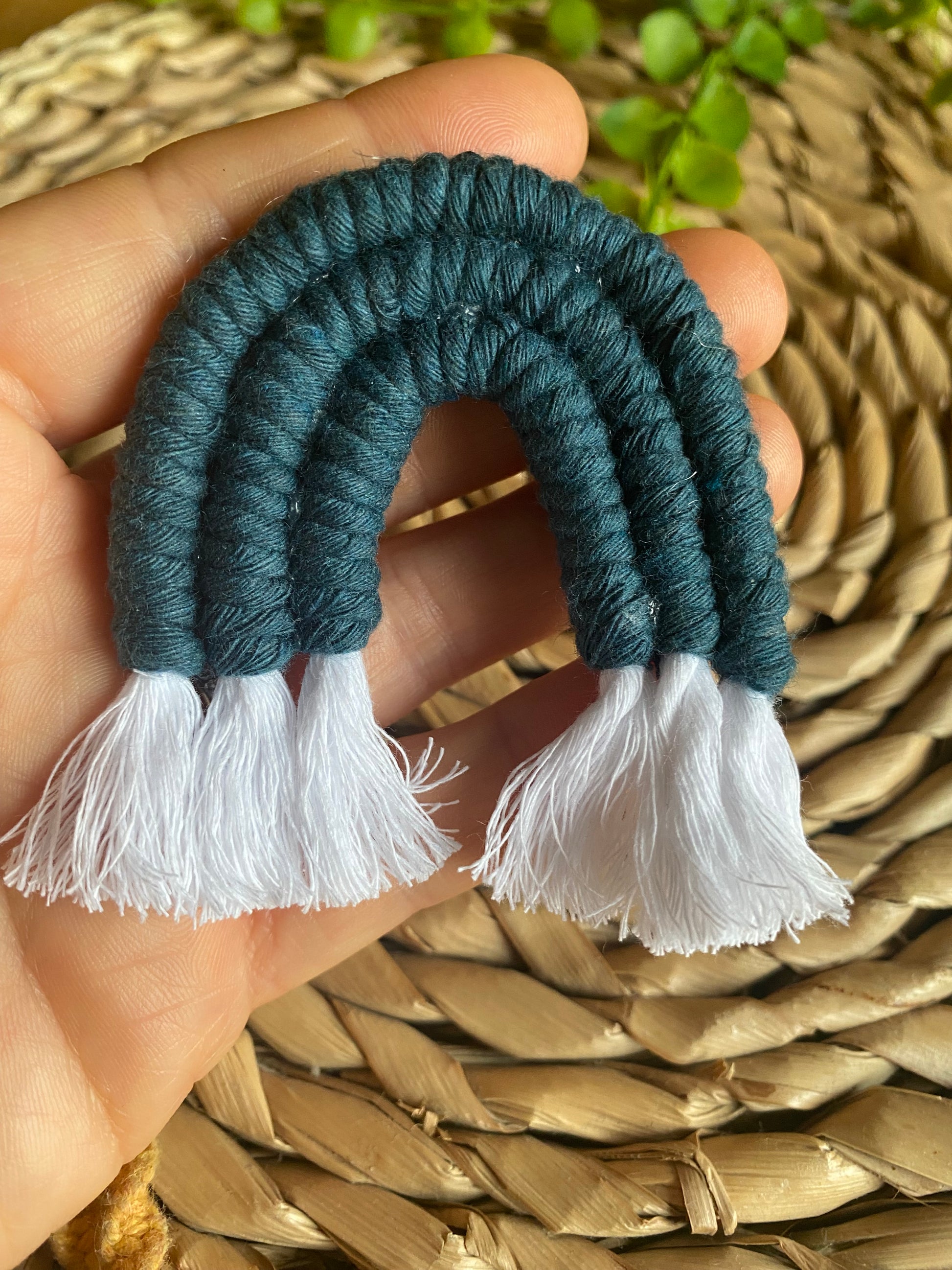 A hand holding a mini macrame rainbow in blue.