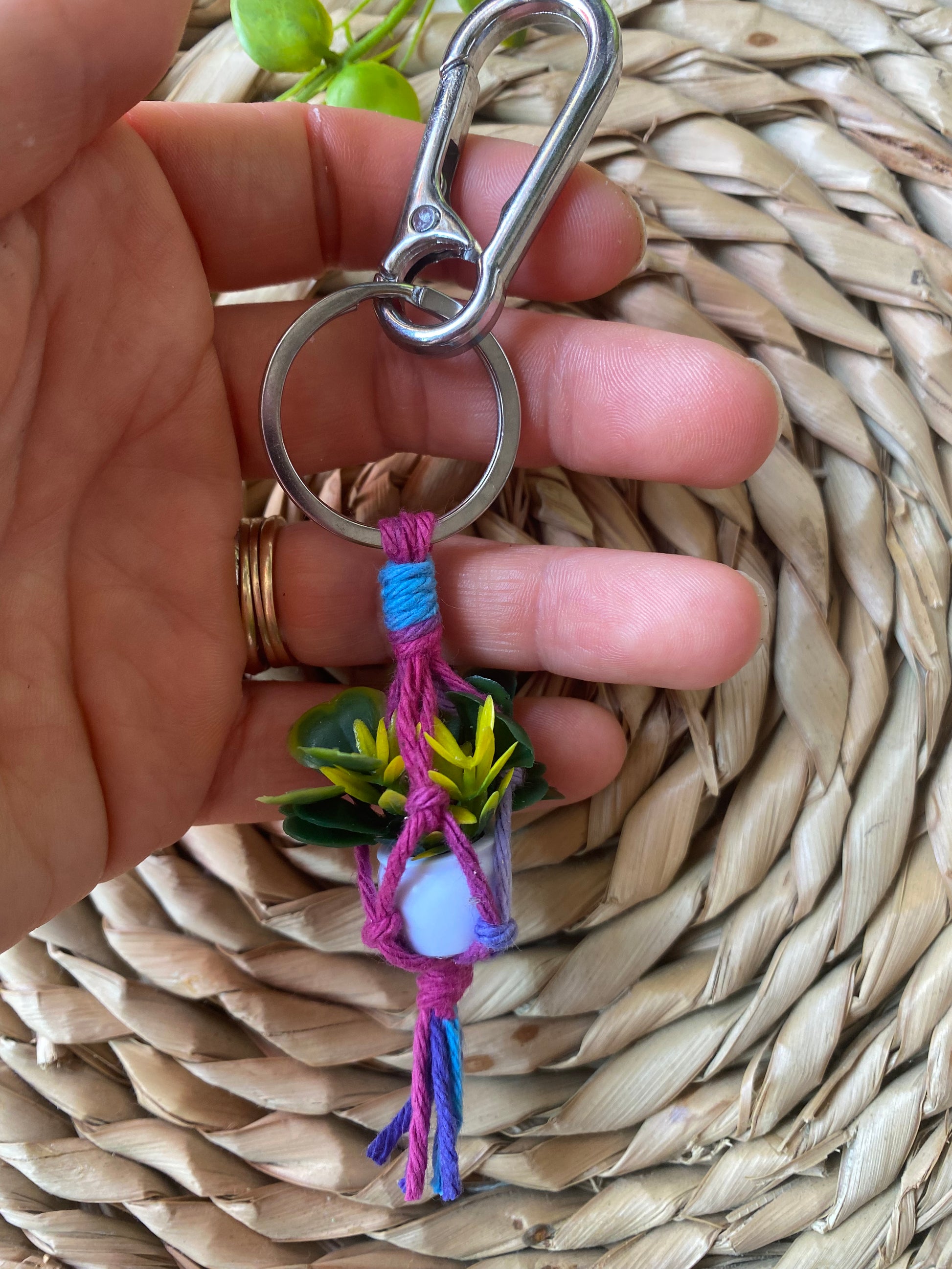 A hand holding a miniature faux plant hanger keyring with metal clasp.