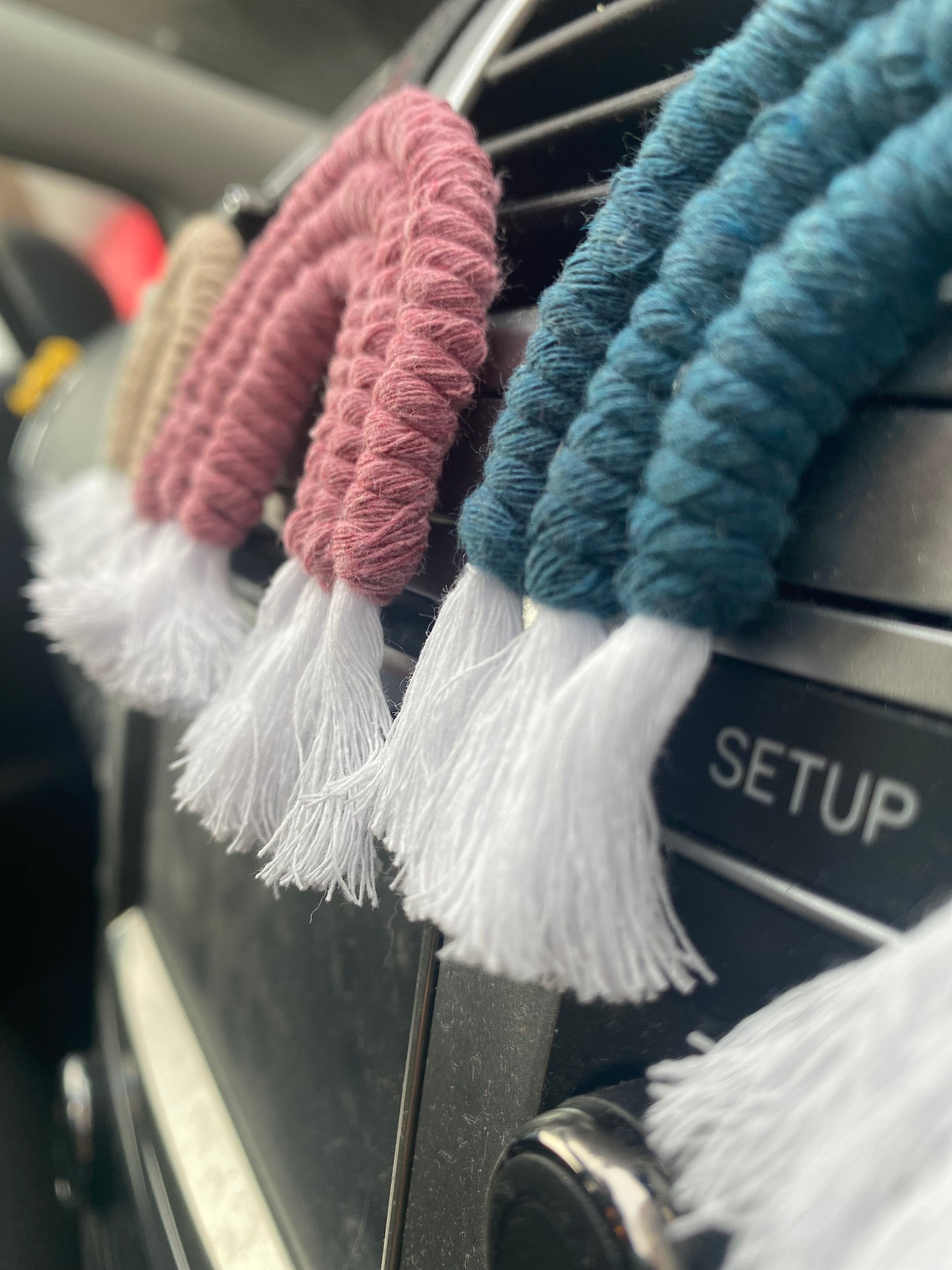 Close up of mini macrame rainbows attached to the car air vent on a black car interior.