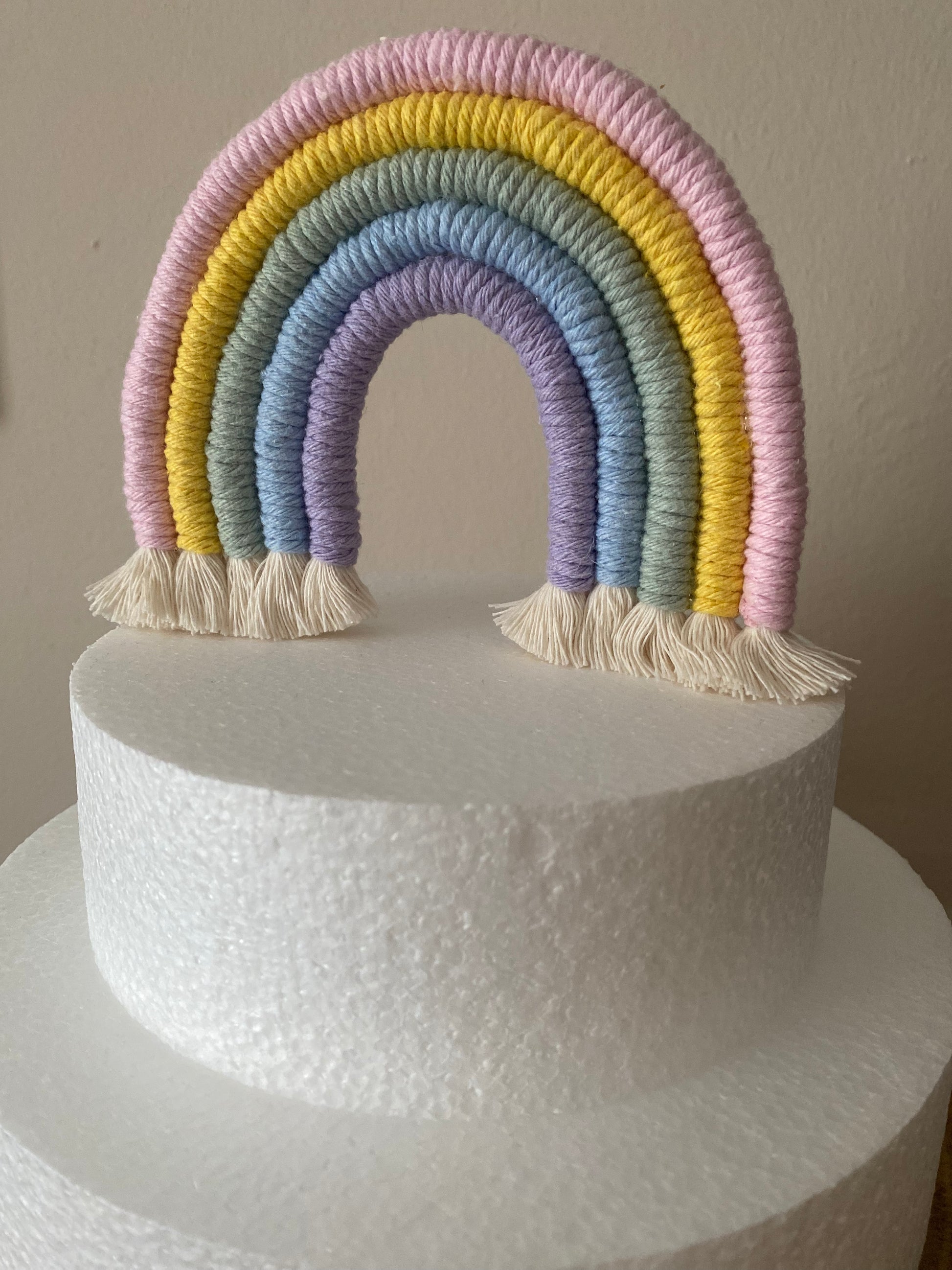 Pastel rainbow macramé cake topper on a white polystyrene cake.