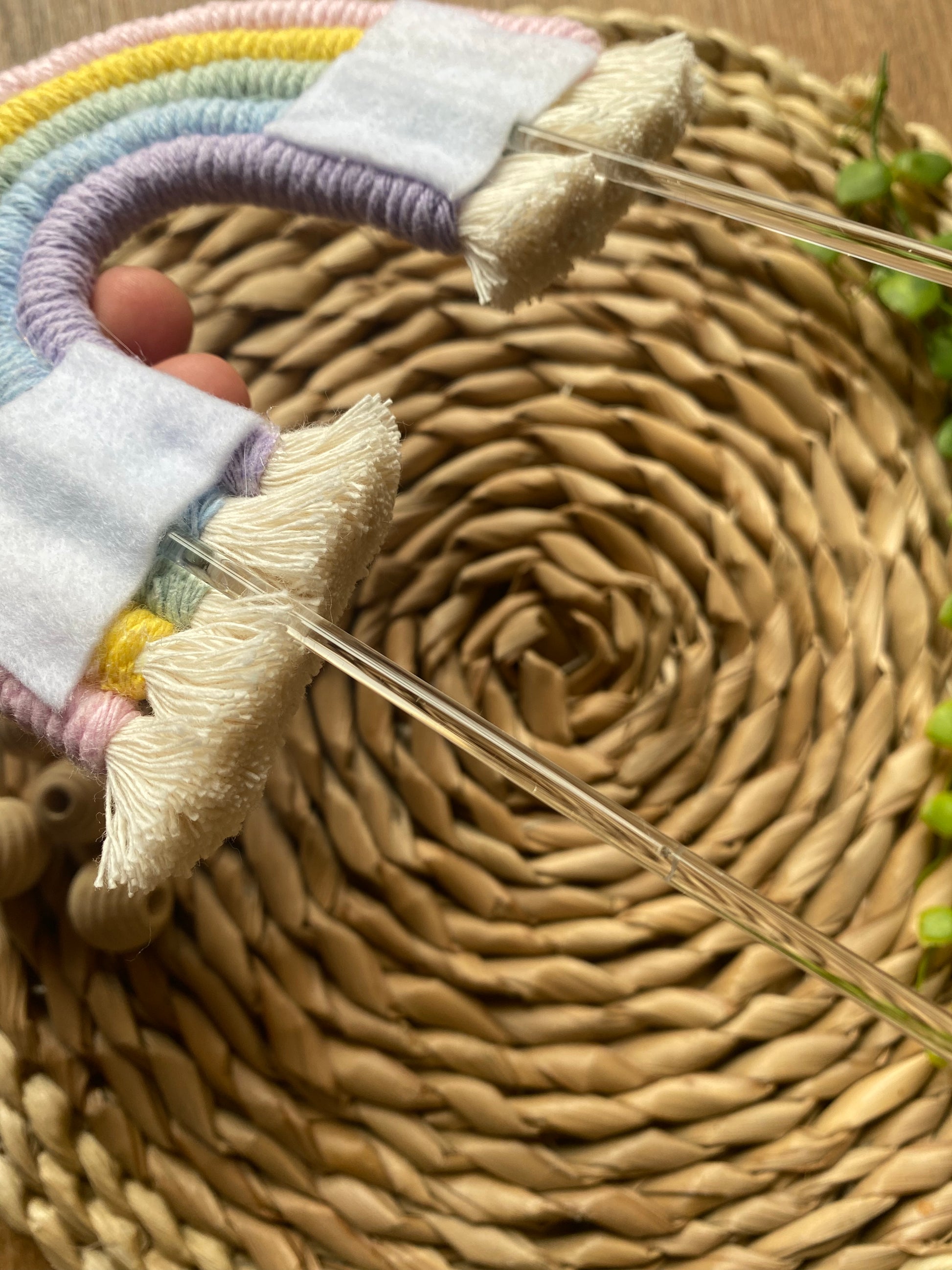 Reverse side of a pastel rainbow macramé cake topper with long clear acrylic sticks. The rainbow has short tassels, and white felt patches where the acrylic sticks attach.