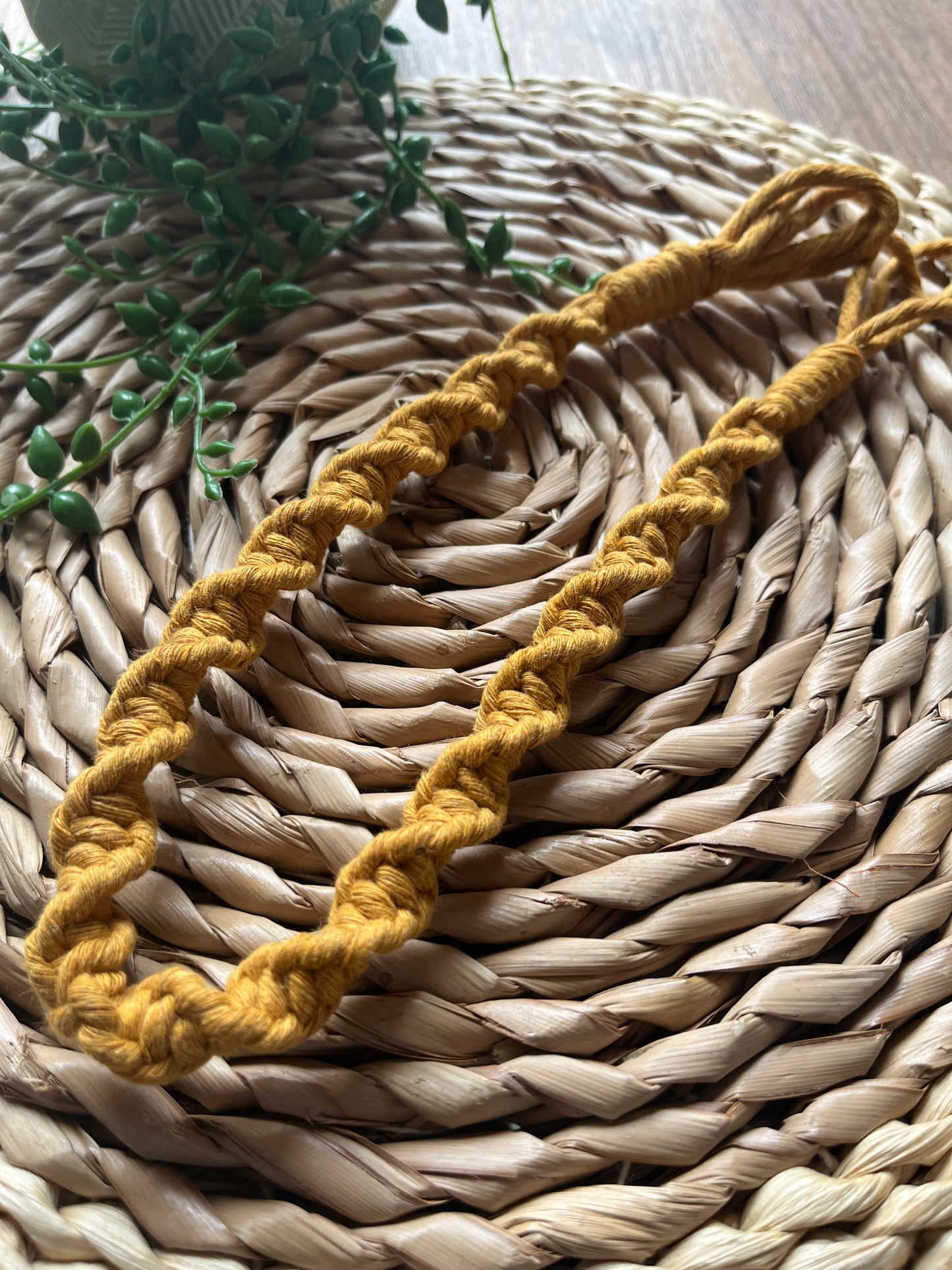 Macrame plant hanger extension in mustard yellow, on a woven mat