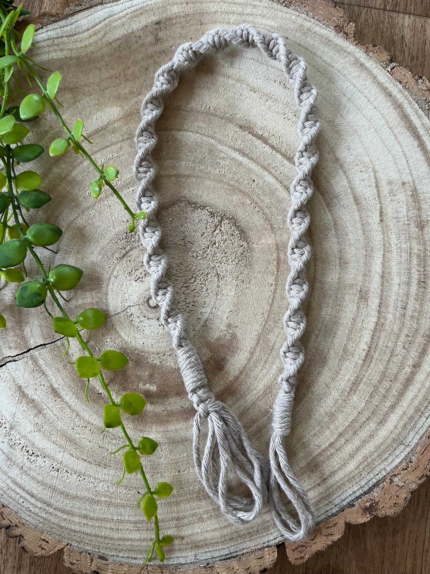A twisted, beige Macra-Made-With-Love macrame indoor plant hanger extension, crafted from recycled cotton, rests on a wooden circular surface.