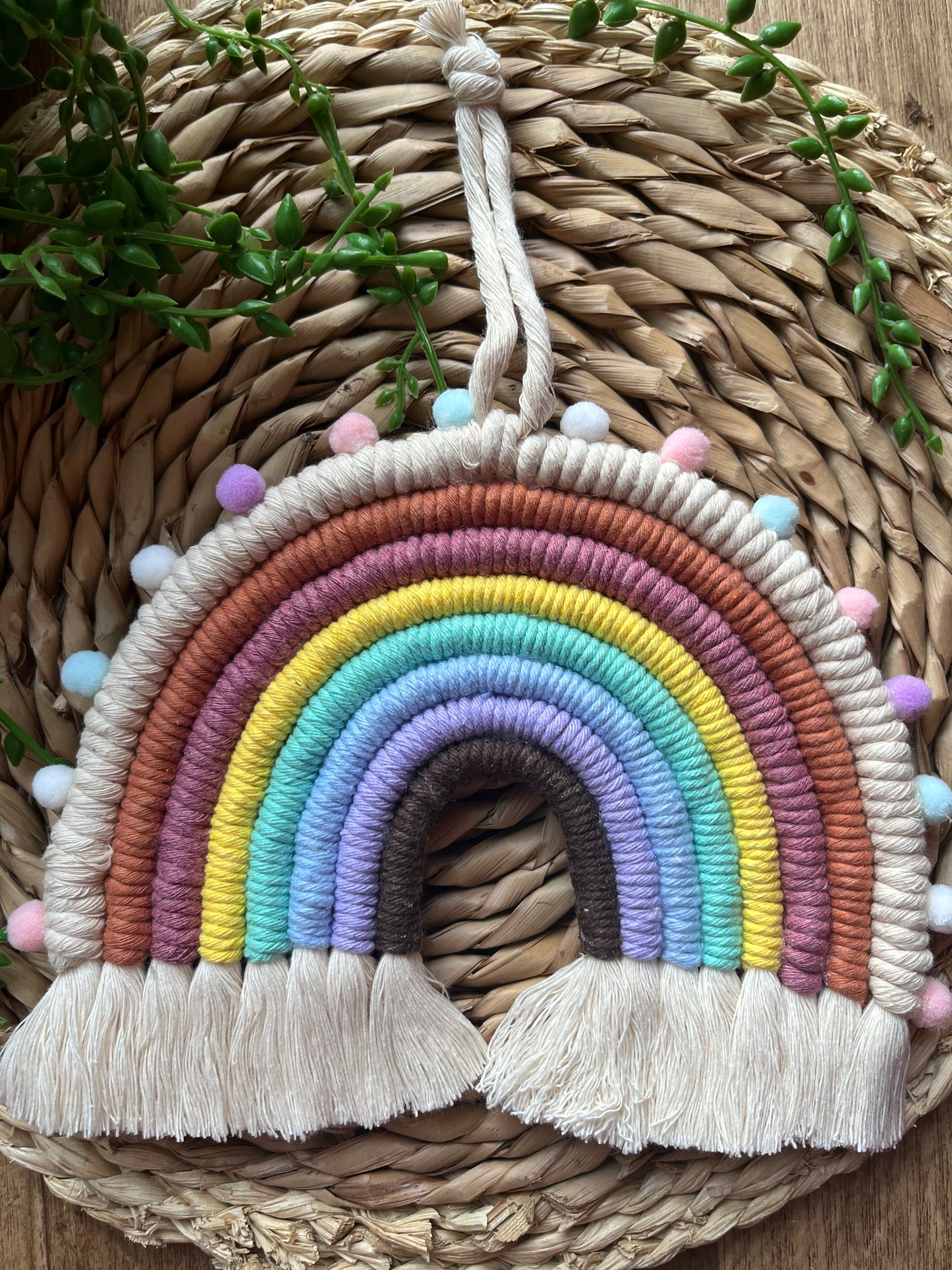 Large multicoloured macrame rainbow made with recycled cotton and finished with small pom poms.