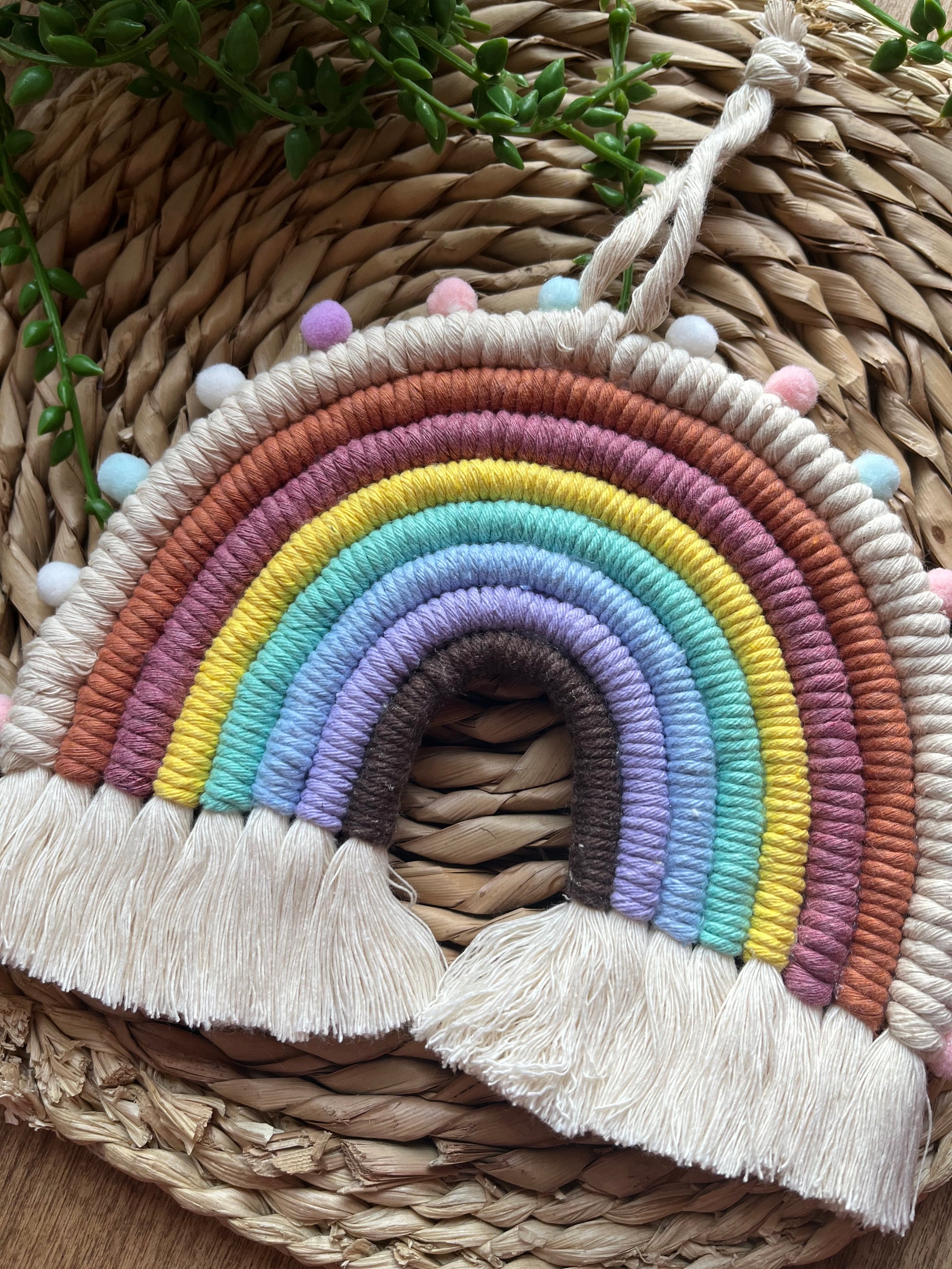 Handmade macrame rainbow wall hanging, made with pastel shades of recycled cotton and finished with small pom poms around the edge.