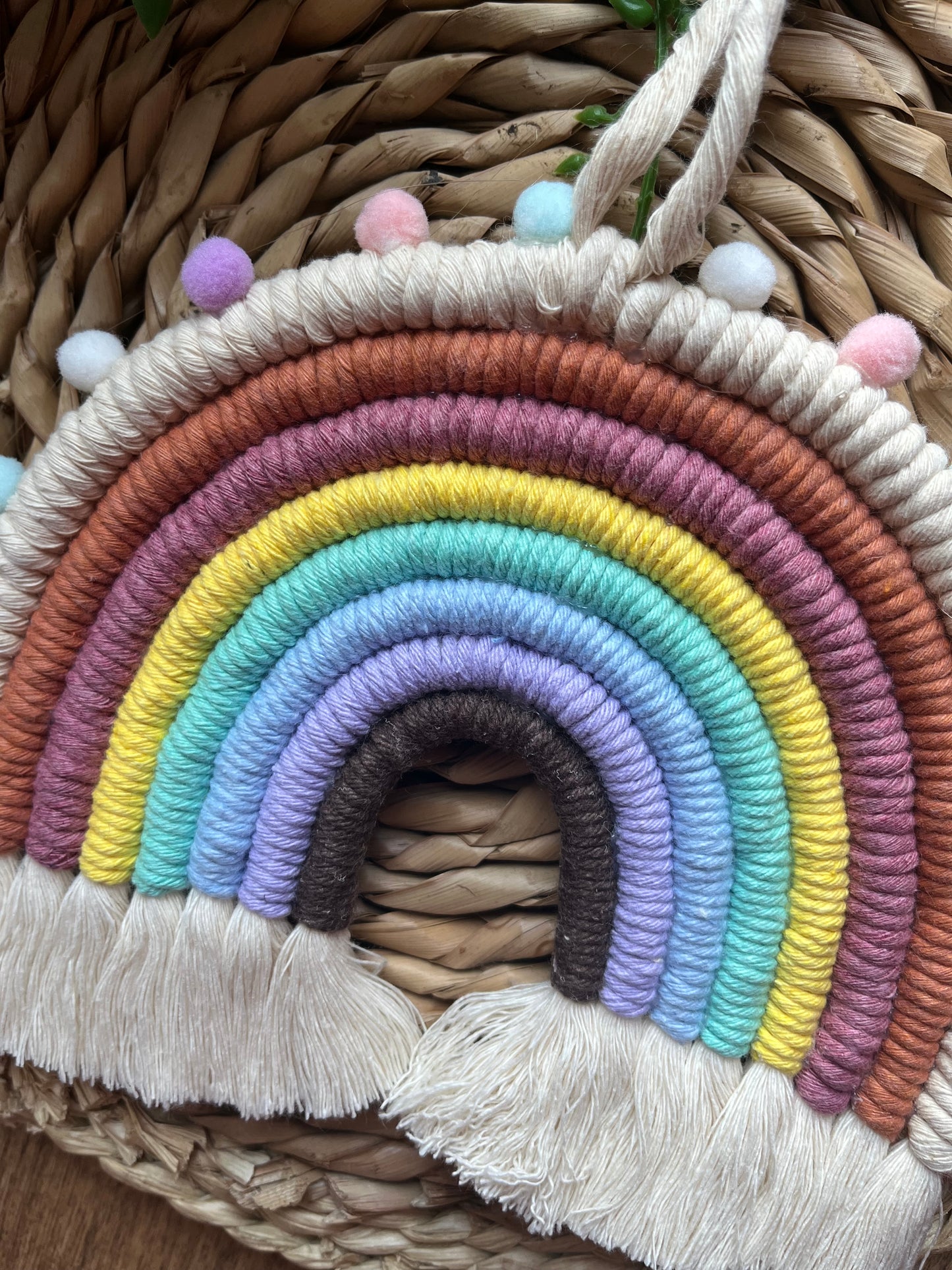 Handmade macrame rainbow wall hanging, made with pastel shades of recycled cotton and finished with small pom poms around the edge.