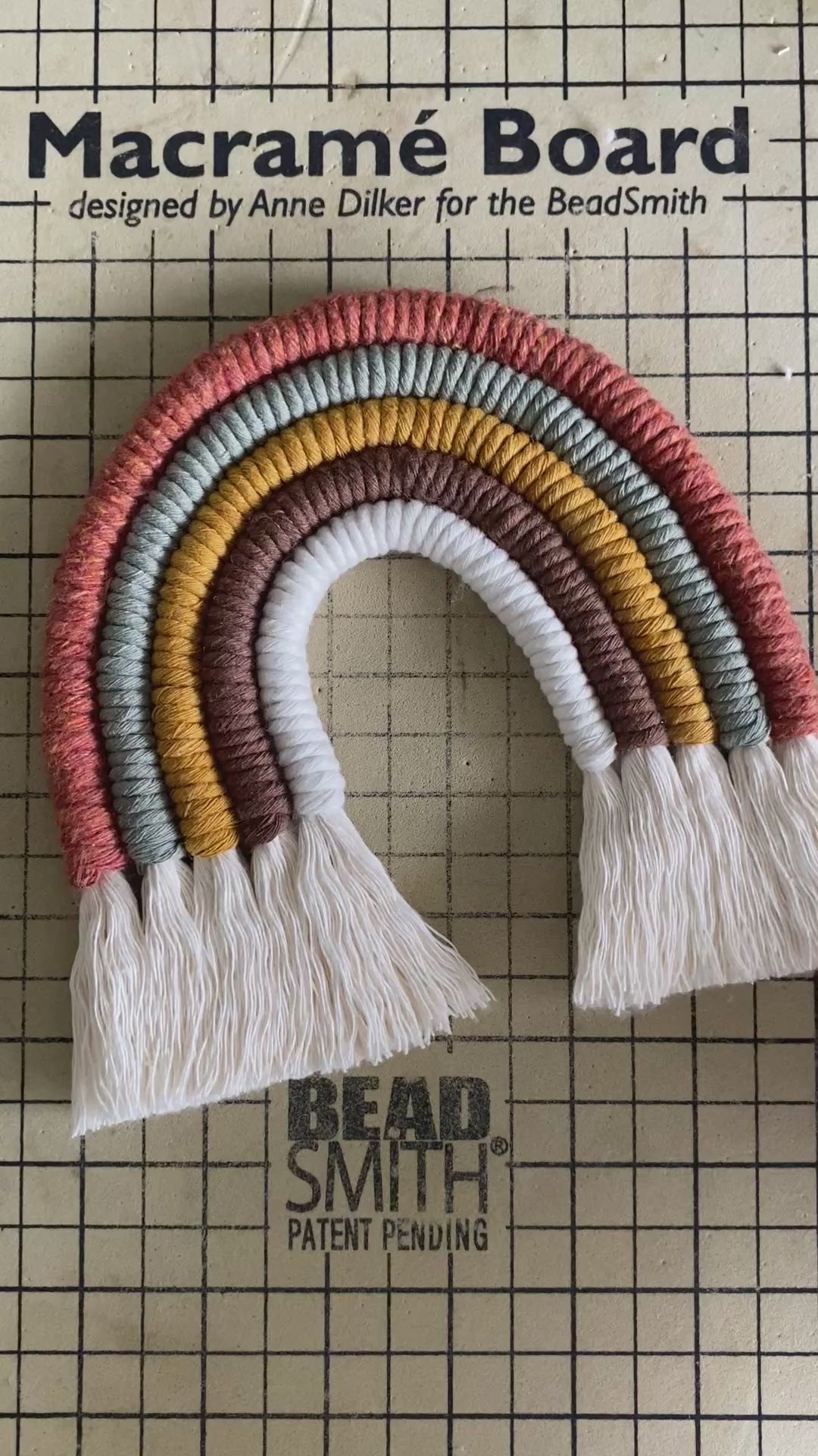 A video showing part of the making process of a macrame rainbow in earthy tones.
