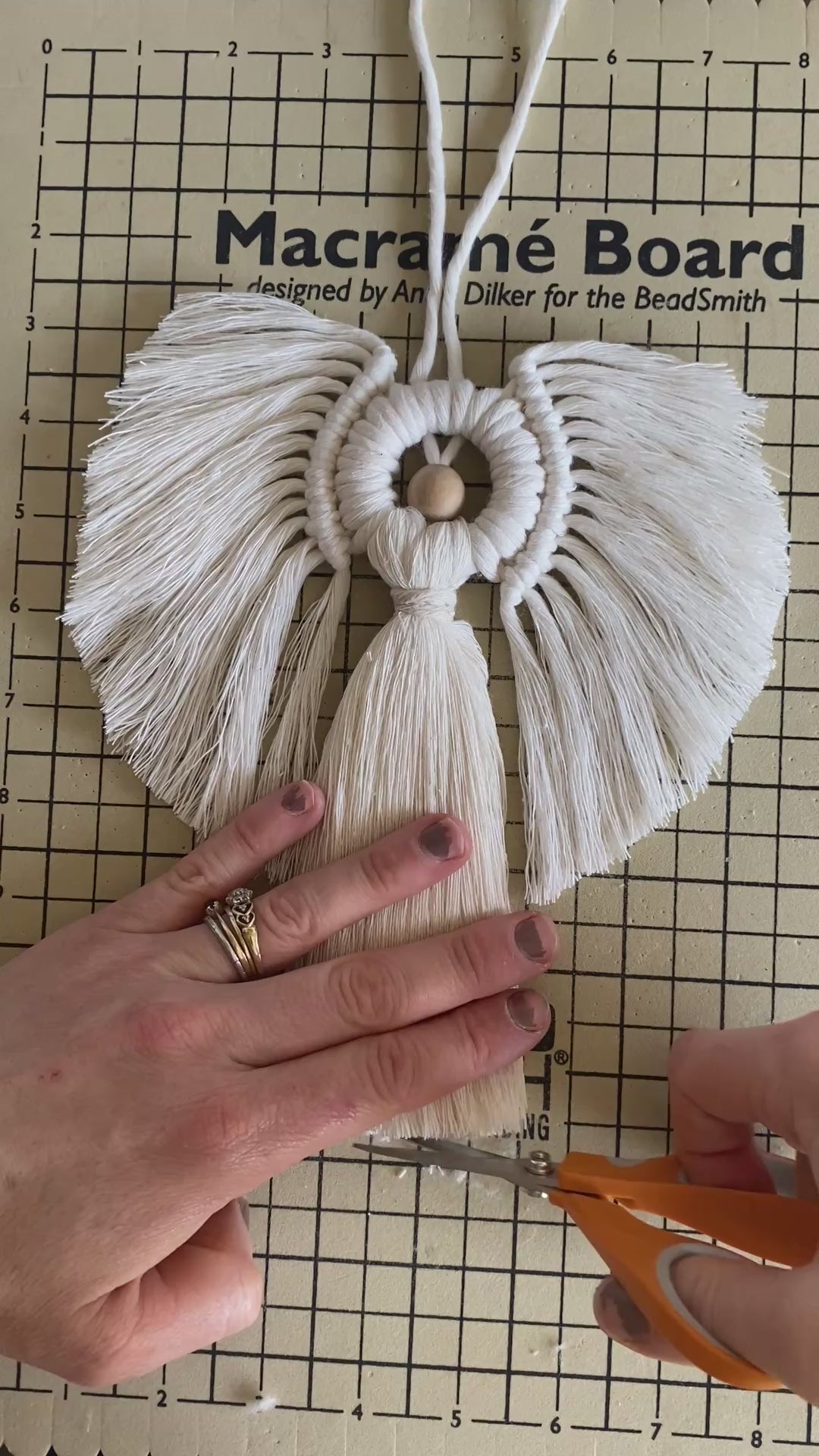 A video showing part of the making process of a macrame angel decoration made with natural cotton yarns and a wooden bead.