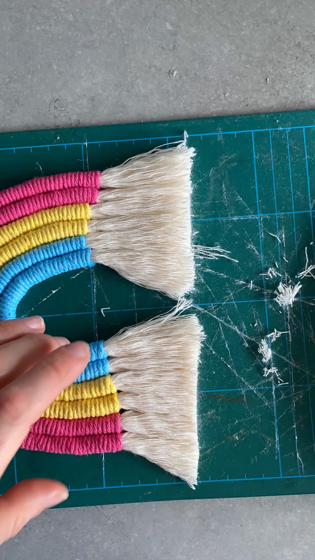 A video showing part of the making process of a macrame rainbow in pink blue and yellow.