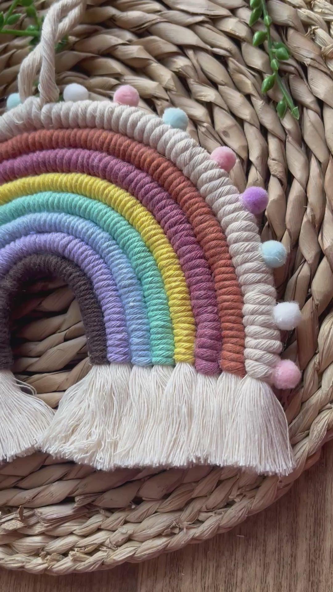Video showing pom pom macrame rainbow, handmade using pastel shades of recycled cotton and finished with small pom poms.