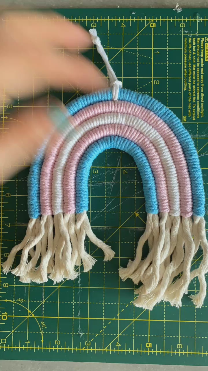 A video showing part of the making process of a macrame rainbow in the colours of the pride trans flag.