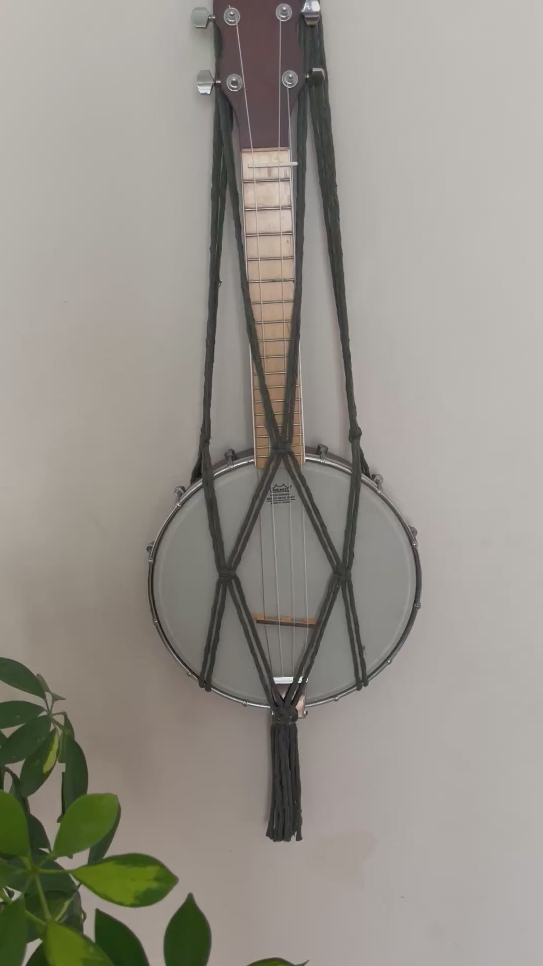 A video showing up close details of a macrame banjolele wall hanger made with olive green cotton yarn.