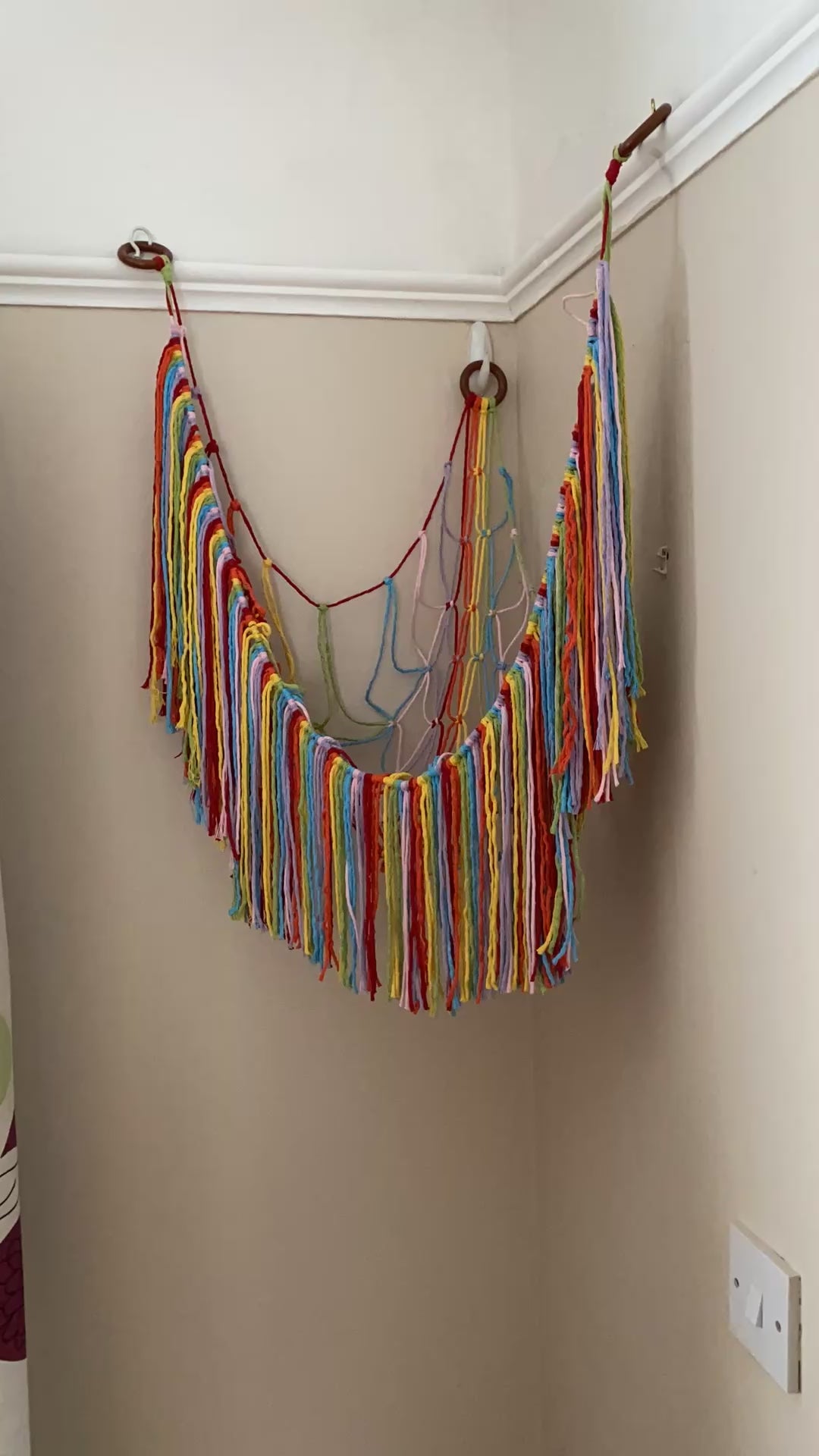 A video showing a woman filling a rainbow toy hammock with soft toys.