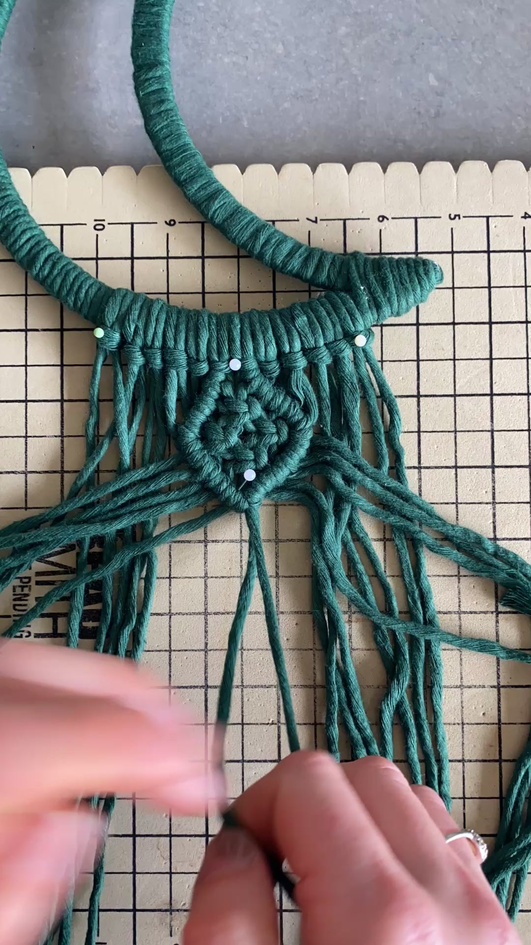 Video showing part of the making process of knotting a macrame moon shaped wall hanging using pine green cotton yarn.
