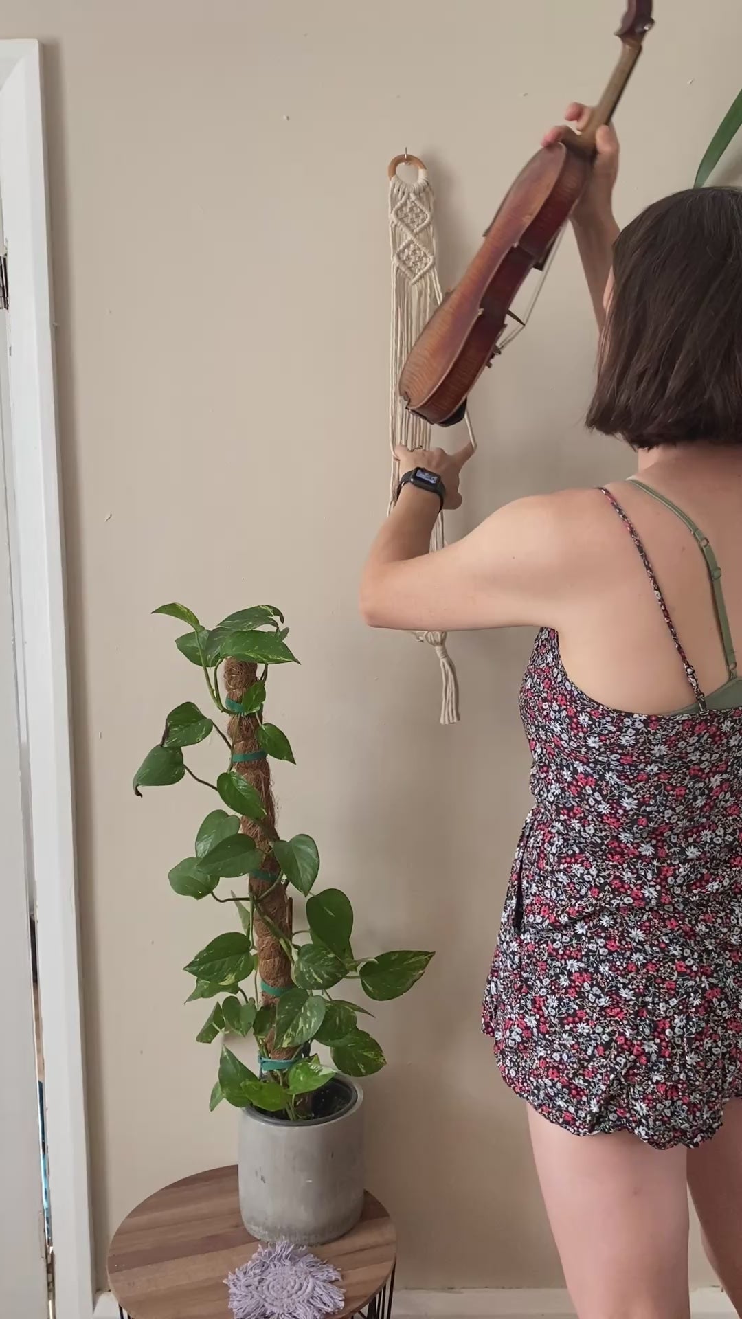 A video showing a woman putting a violin in a macrame wall hanger.